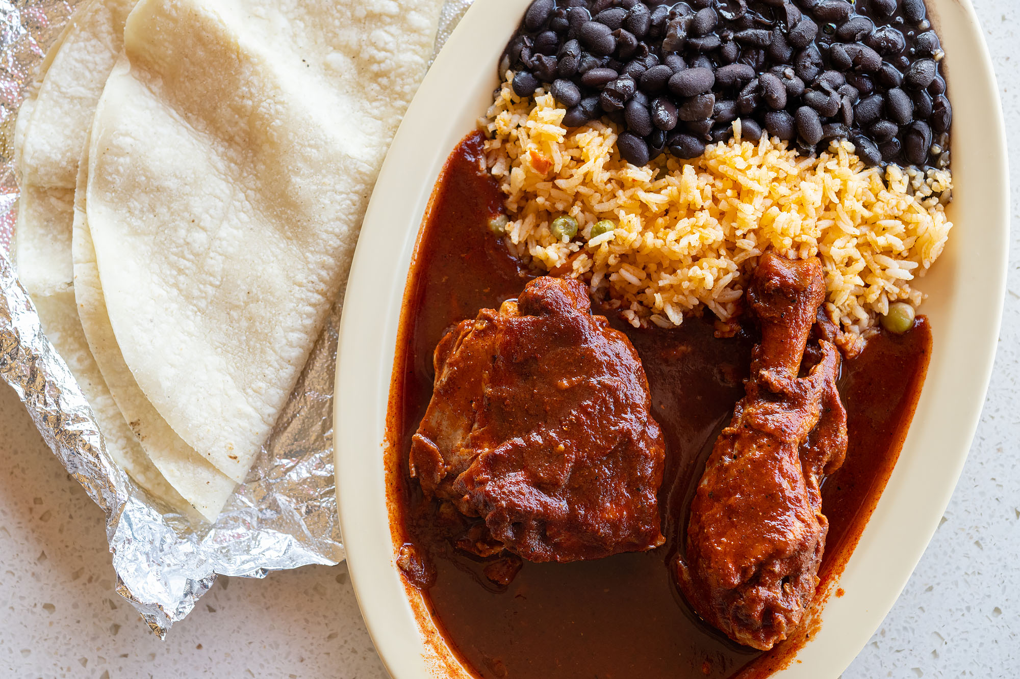 Reddish chicken dish with rice, beans, and tortillas.