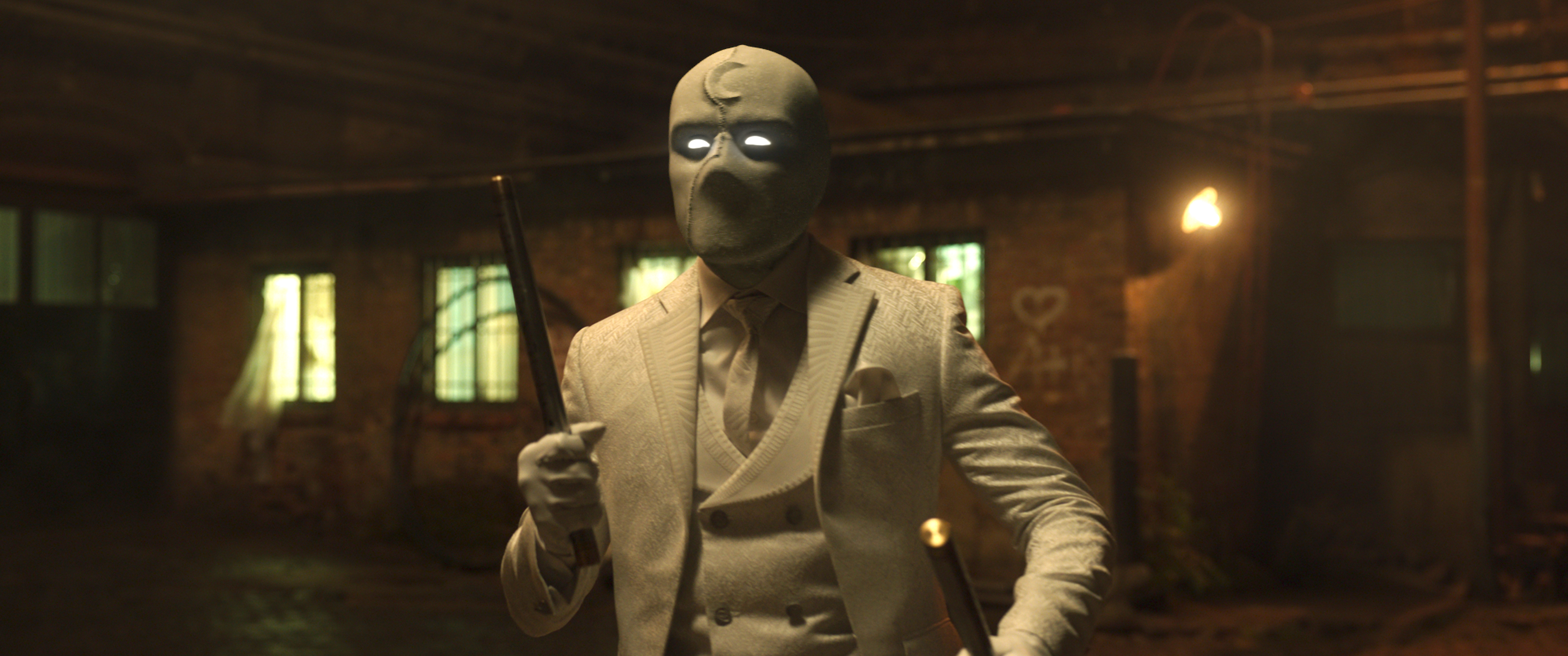 Oscar Isaac as Mr. Knight in Moon Knight — in a stark white suit and cowl, holding up an escrima stick.
