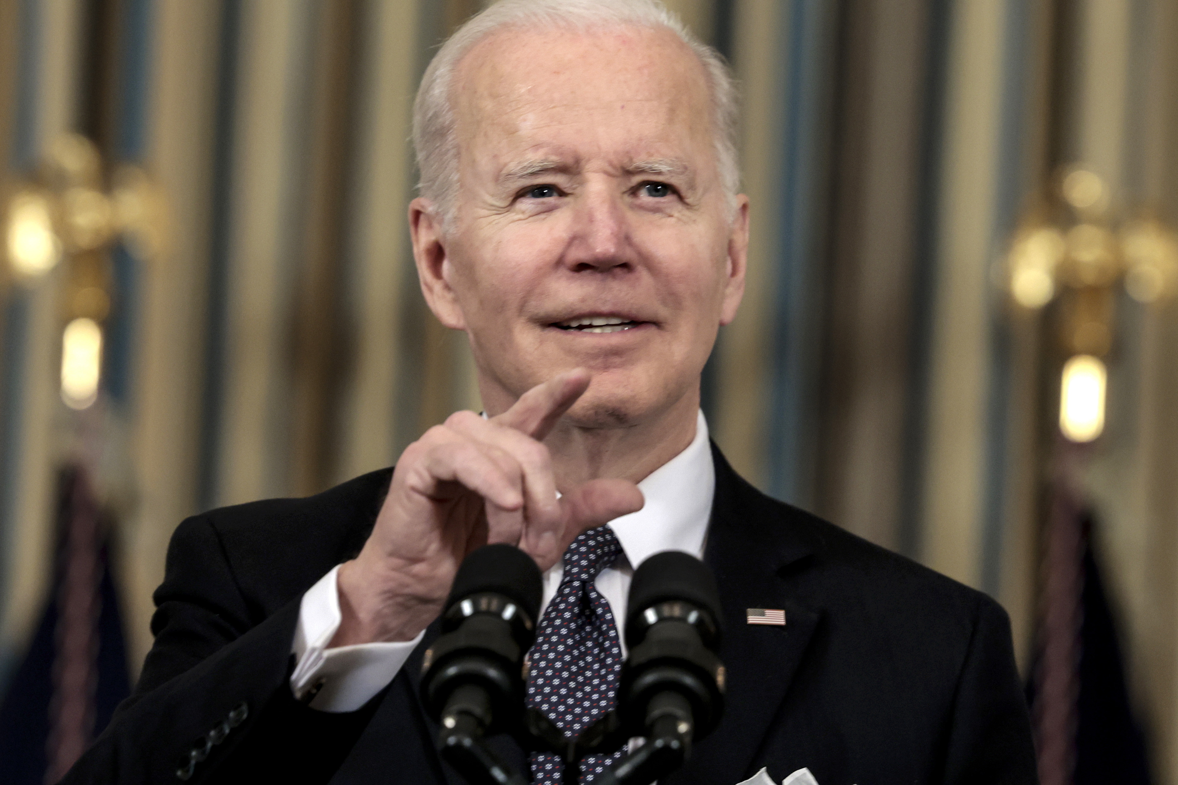 President Joe Biden smiling and pointing from behind a press conference pair of microphones.