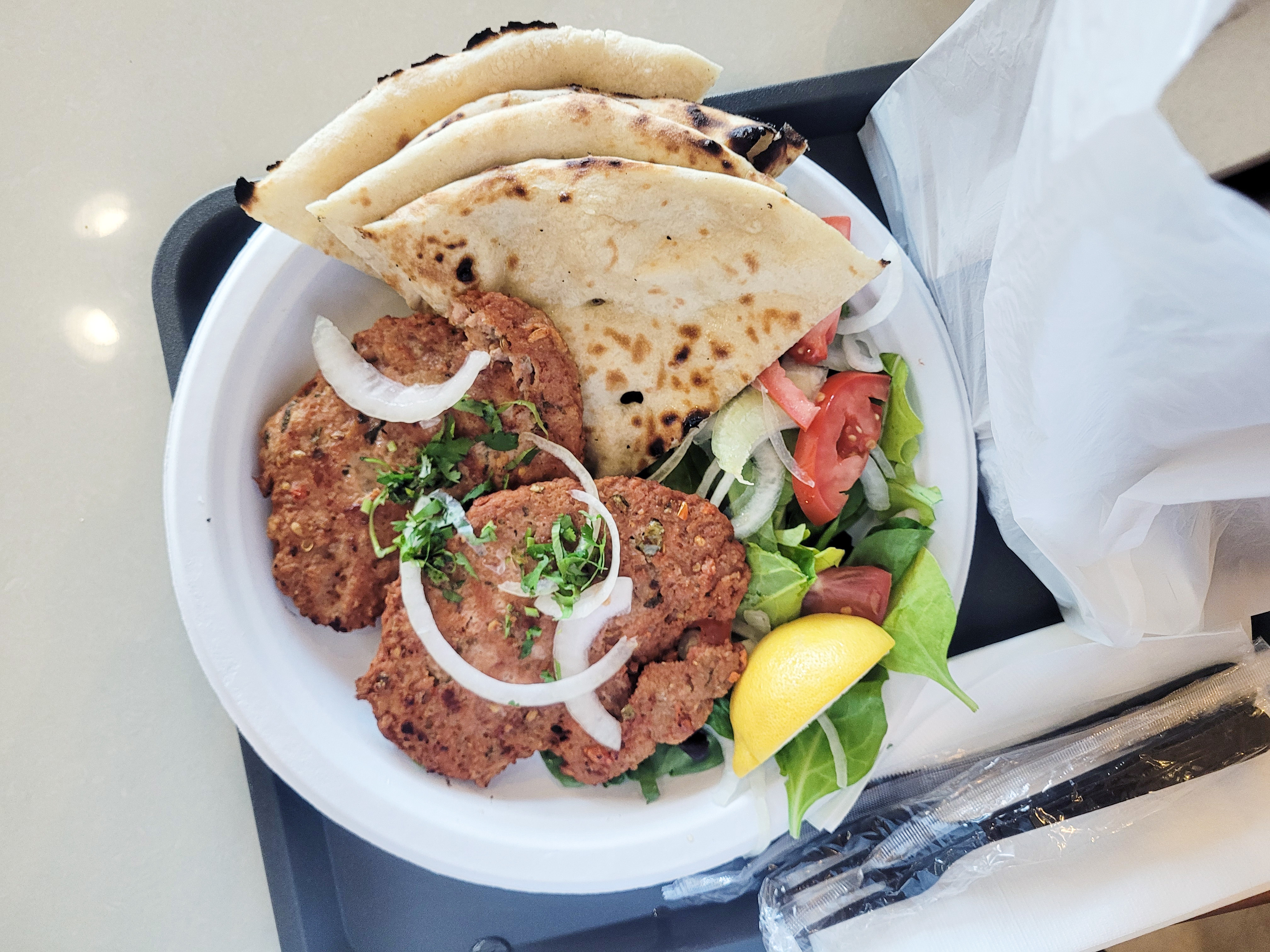 A pair of minced kebabs made from ground beef with various spices in the shape of a patty sit on a plate with naan.