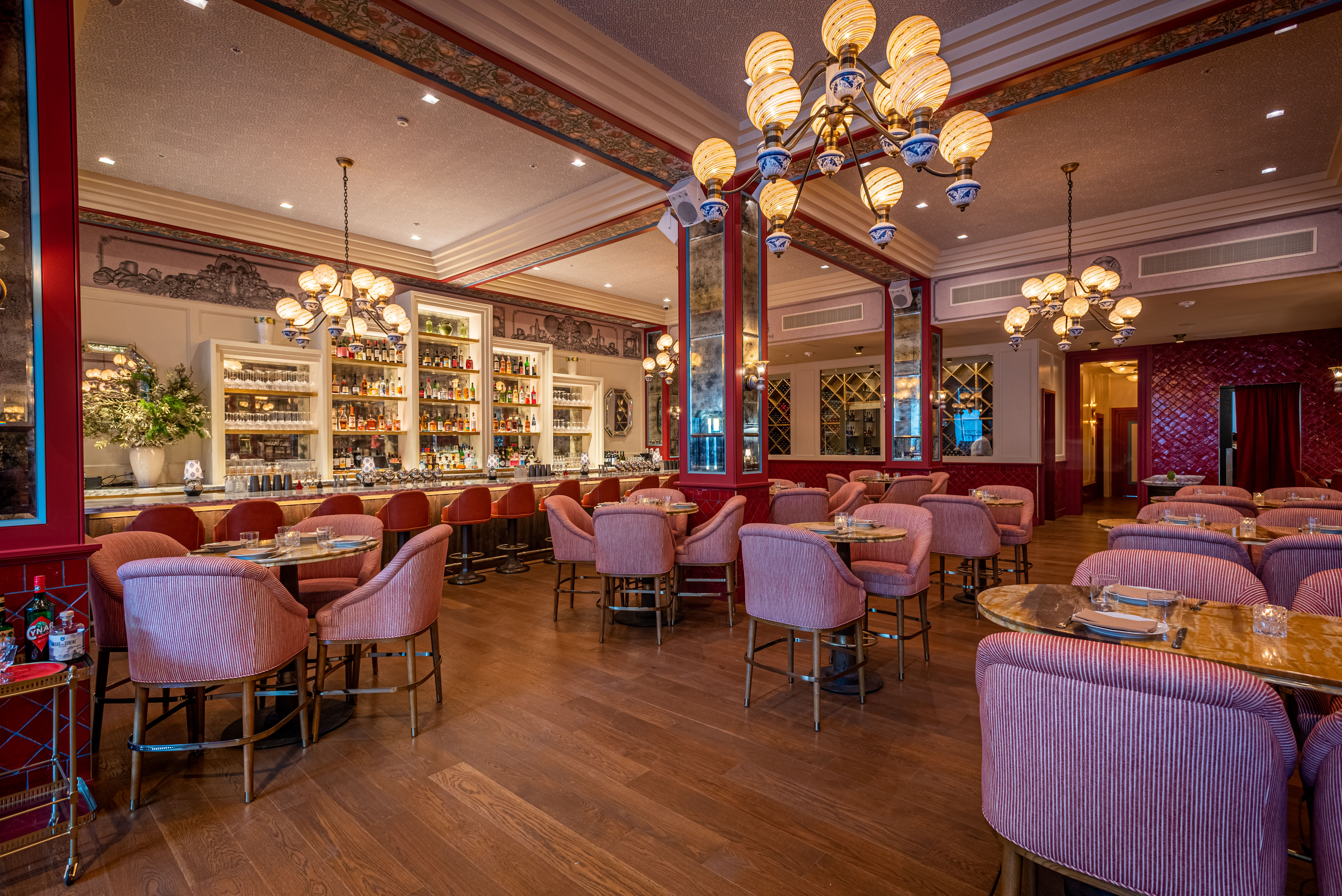 A wide view of a new Italian restaurant with red tones and vintage lighting.