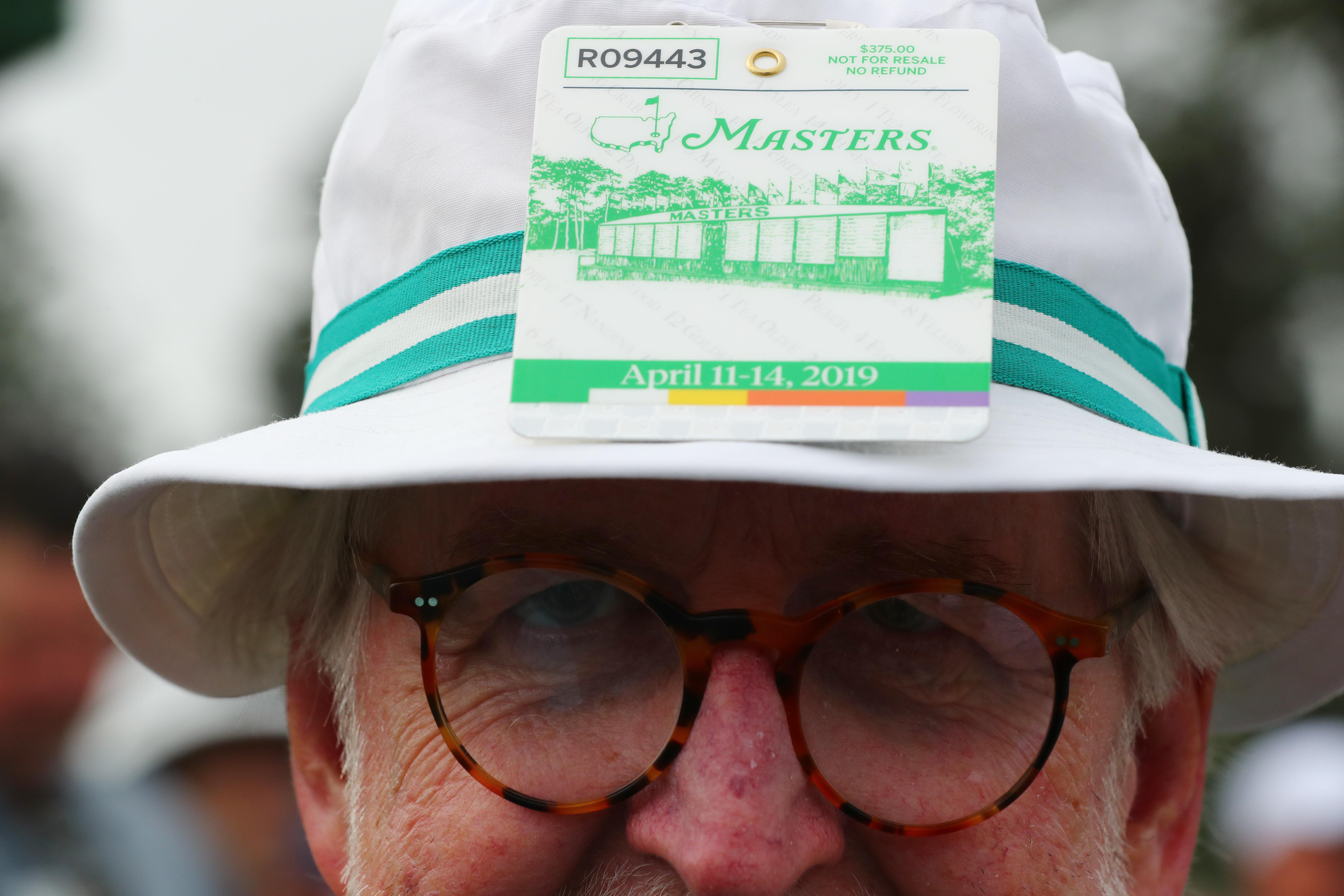A patron wears a Masters badge on his hat during the first round of The Masters golf tournament at Augusta National Golf Club.