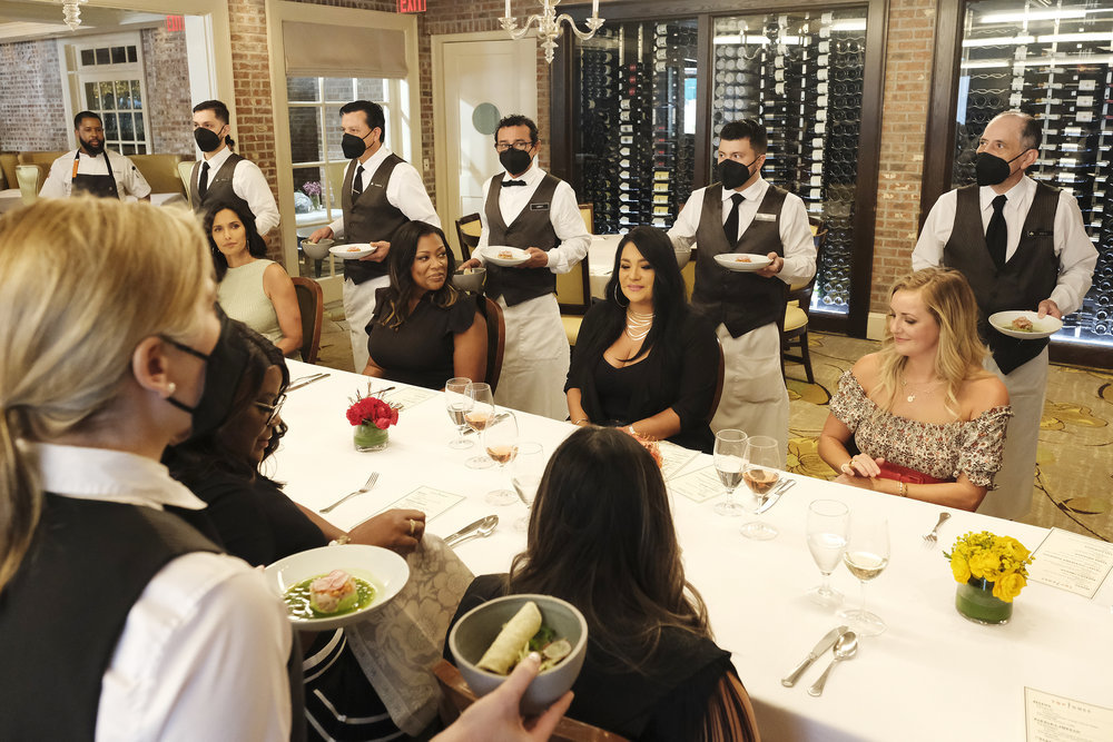 “Top Chef: Houston” host Padma Lakshmi, Dallas chef and “Top Chef” alumna Tiffany Derry, and “Top Chef” Season 16 winner sit at a table where they are served dishes from cheftestants.