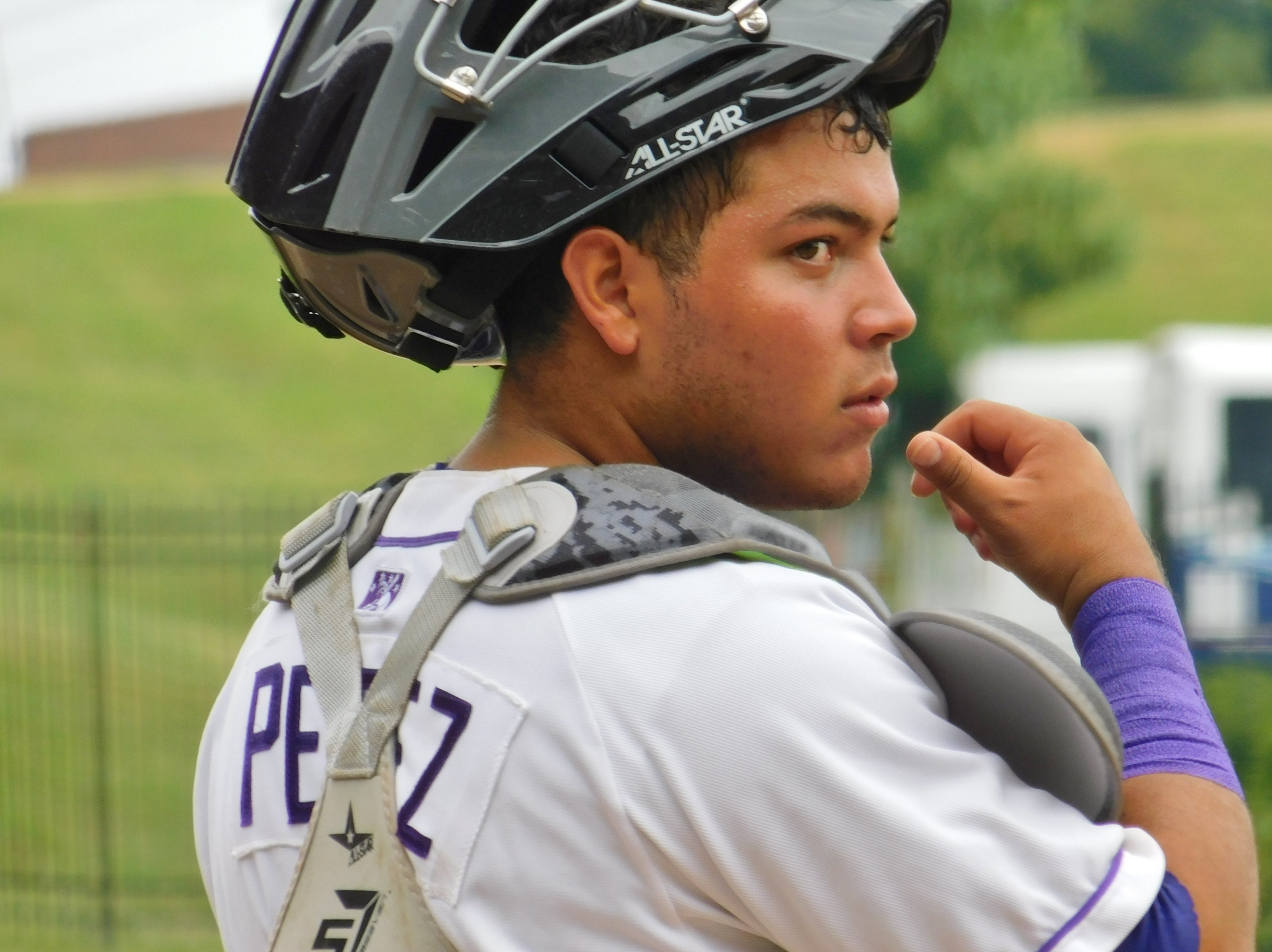 Carlos Pérez stands pictured from the back, wearing a Dash uniform and looking to the right with his catcher’s mask pulled back