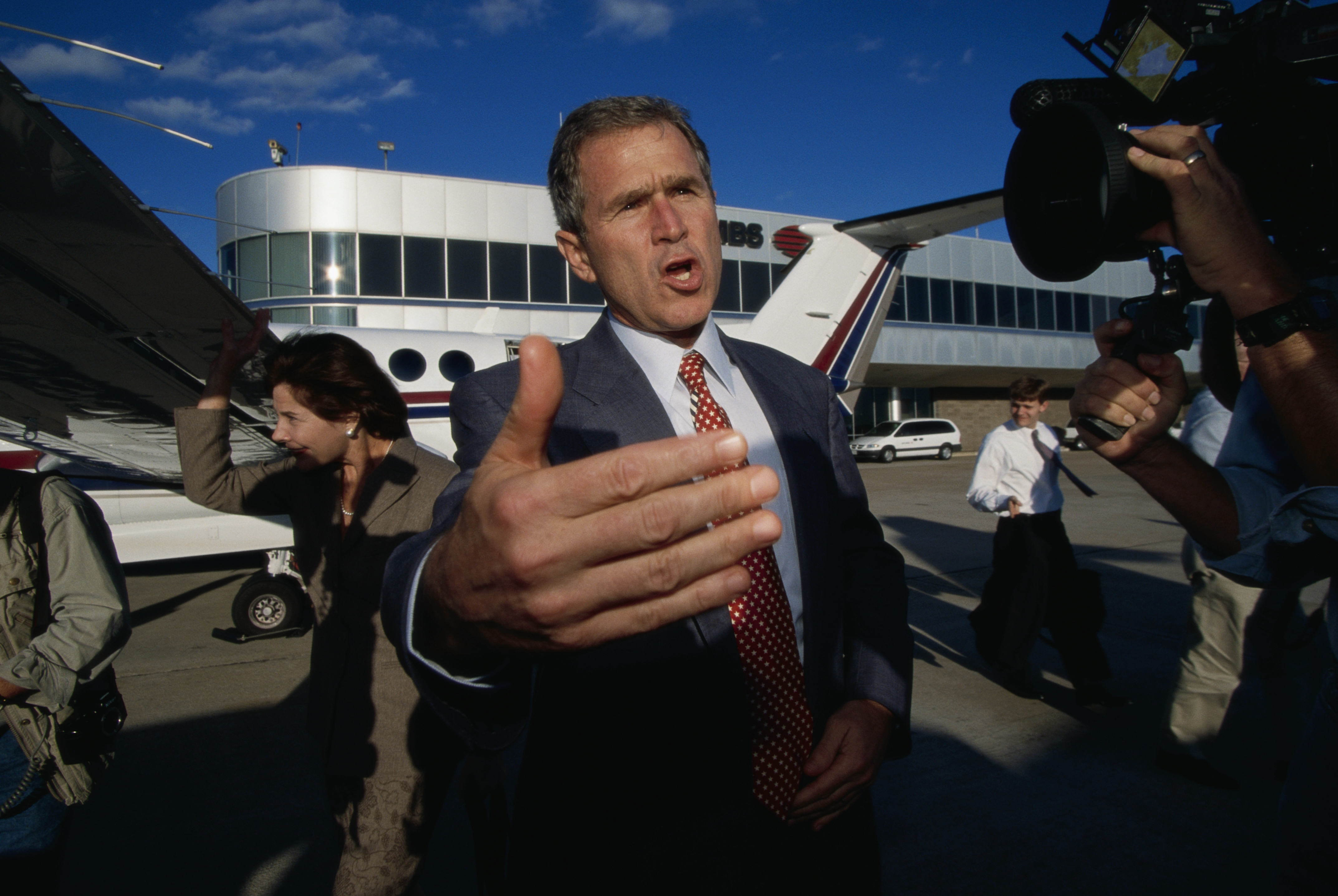 George W. Bush talks, gesturing in front of a camera at the Dallas airport in 1998.