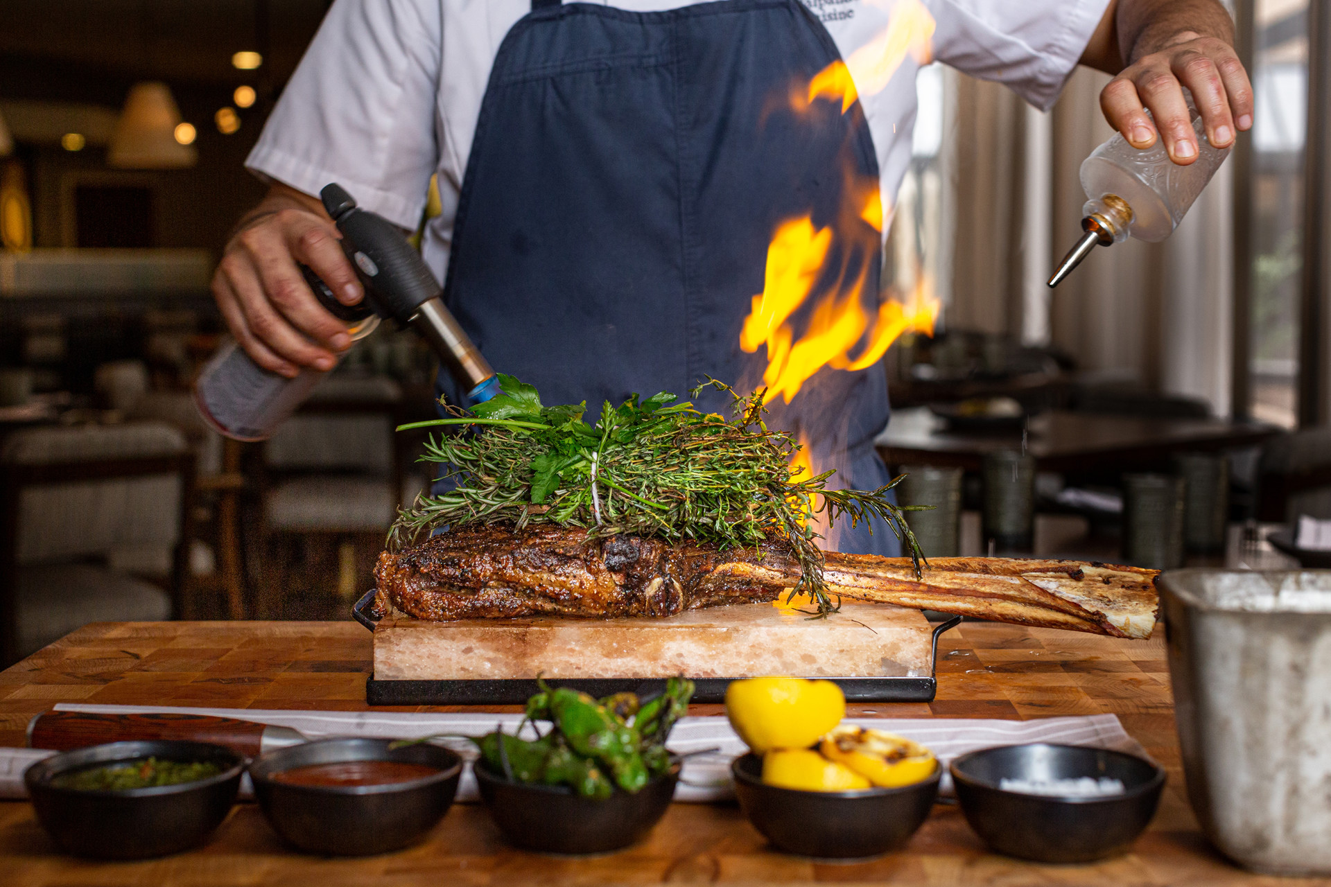 A chef sets a tomahawk on fire using a torch.