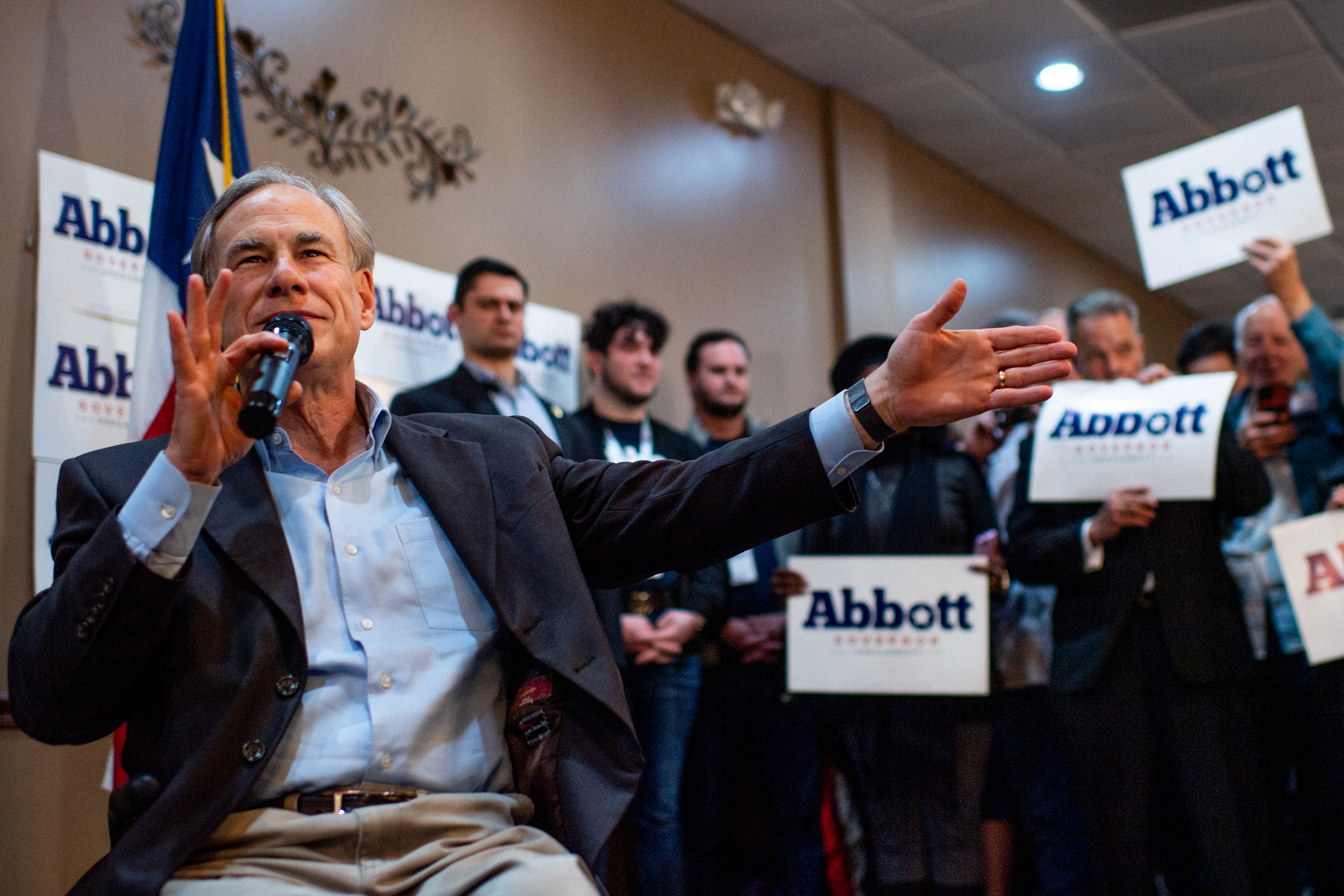 A man with a microphone in front of a crowd of men with “Abbott” campaign signs