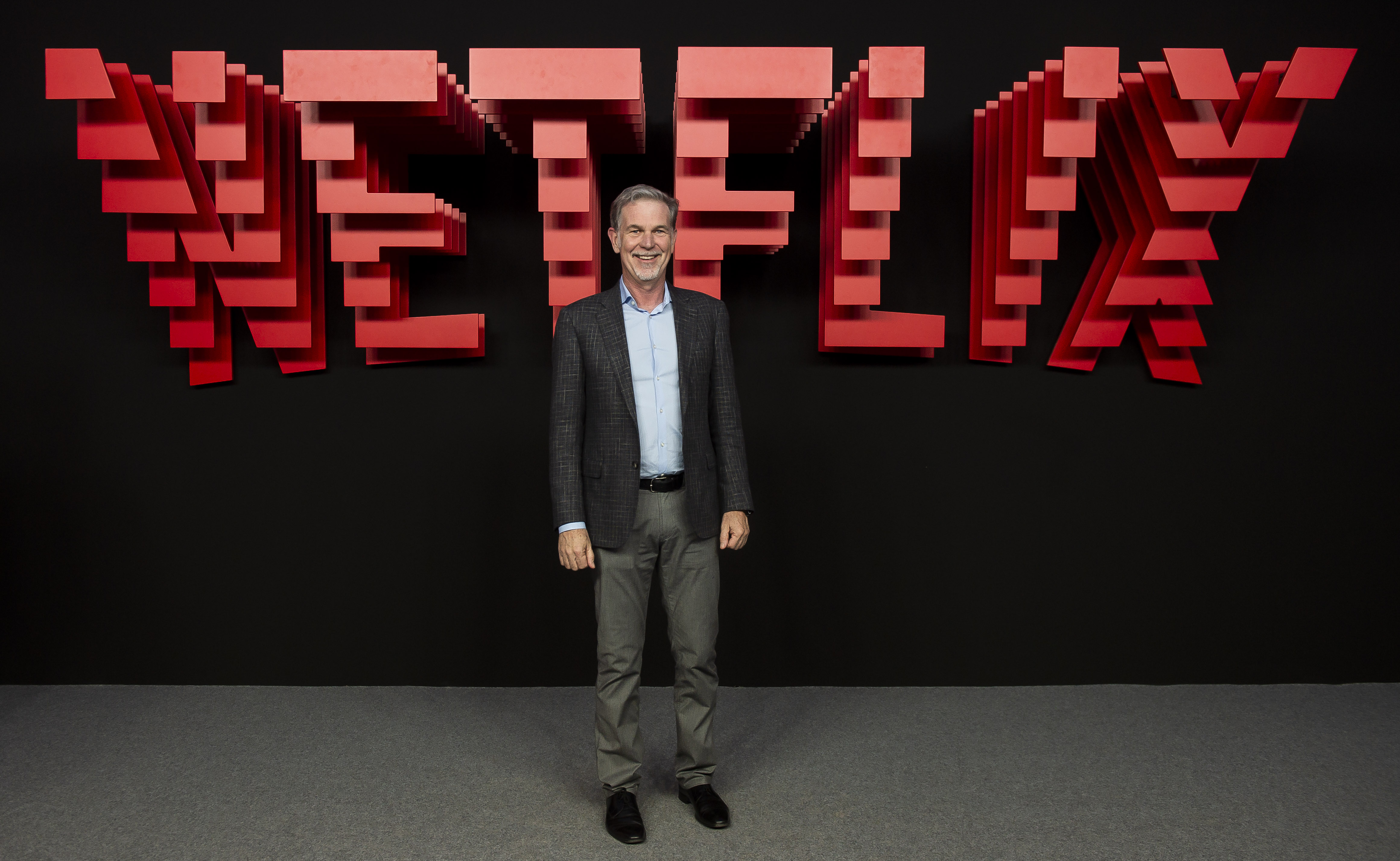 Reed Hastings standing in front of a large sign that says “Netflix.”