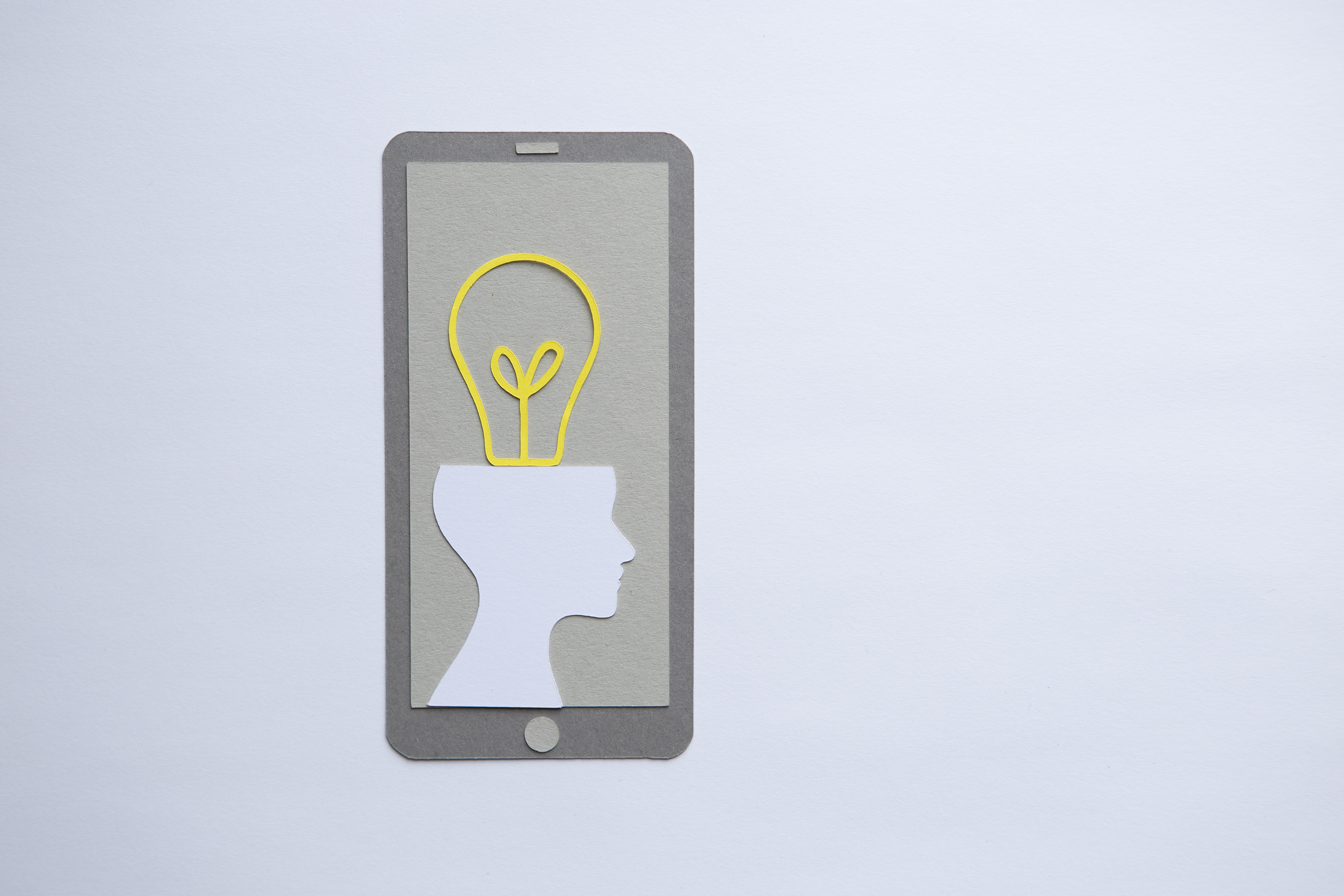 Paper cut-out of a phone, featuring a silhouette of a human head attached to a yellow lightbulb.