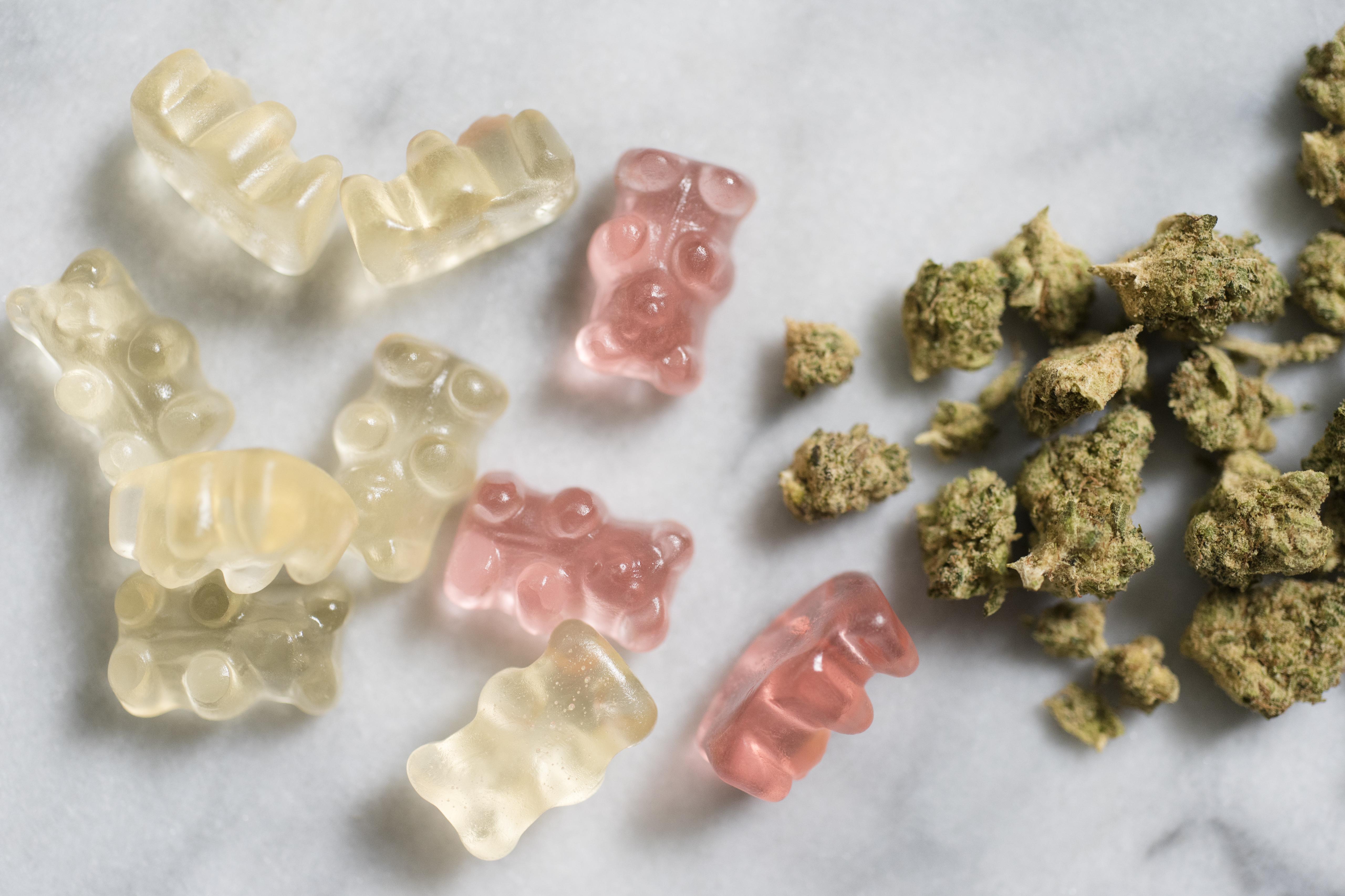 Gummy bears and cannabis scattered on a white marble counter.