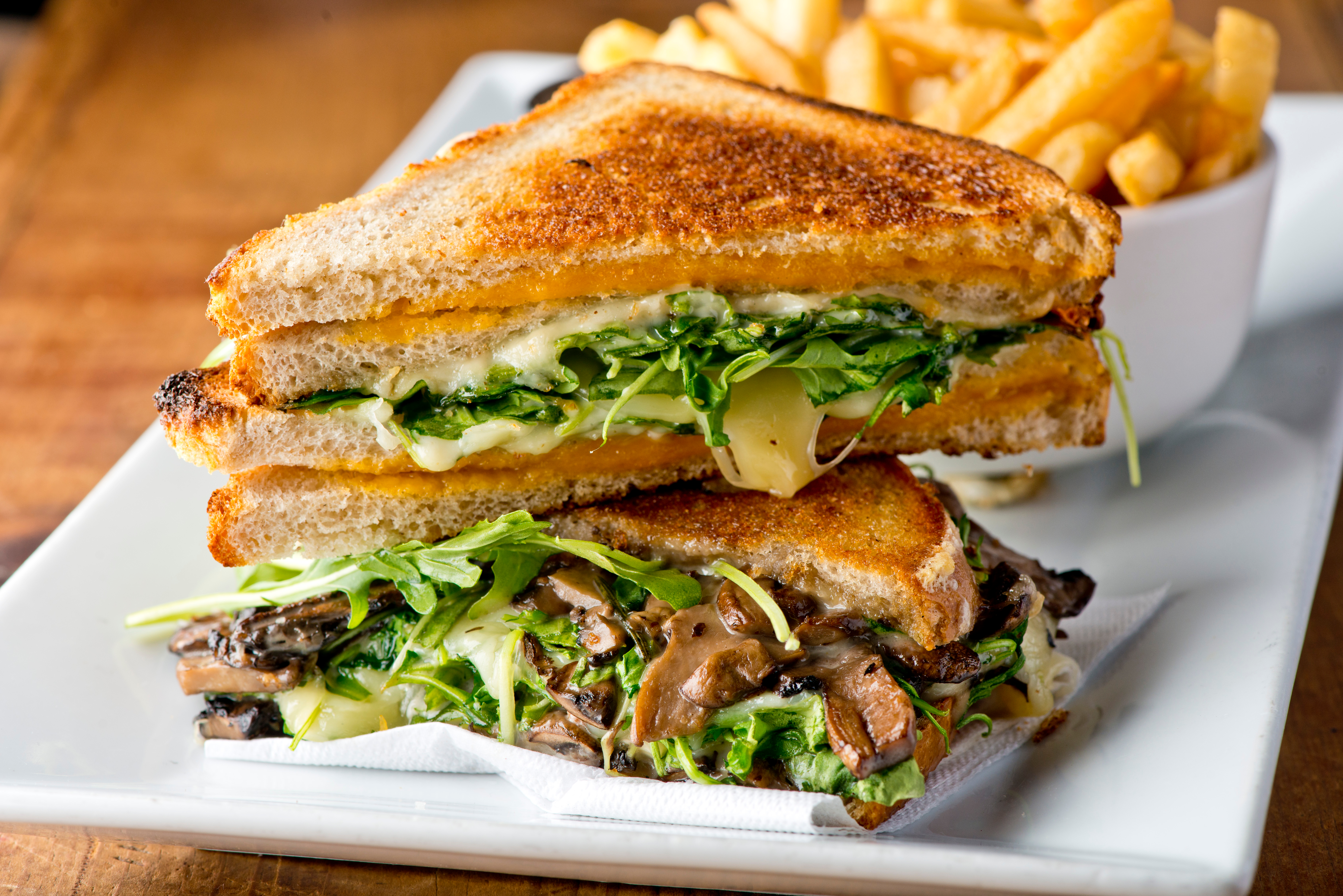Sandwich with mushrooms, arugula, and melted cheese cut in half and displayed on a plate.