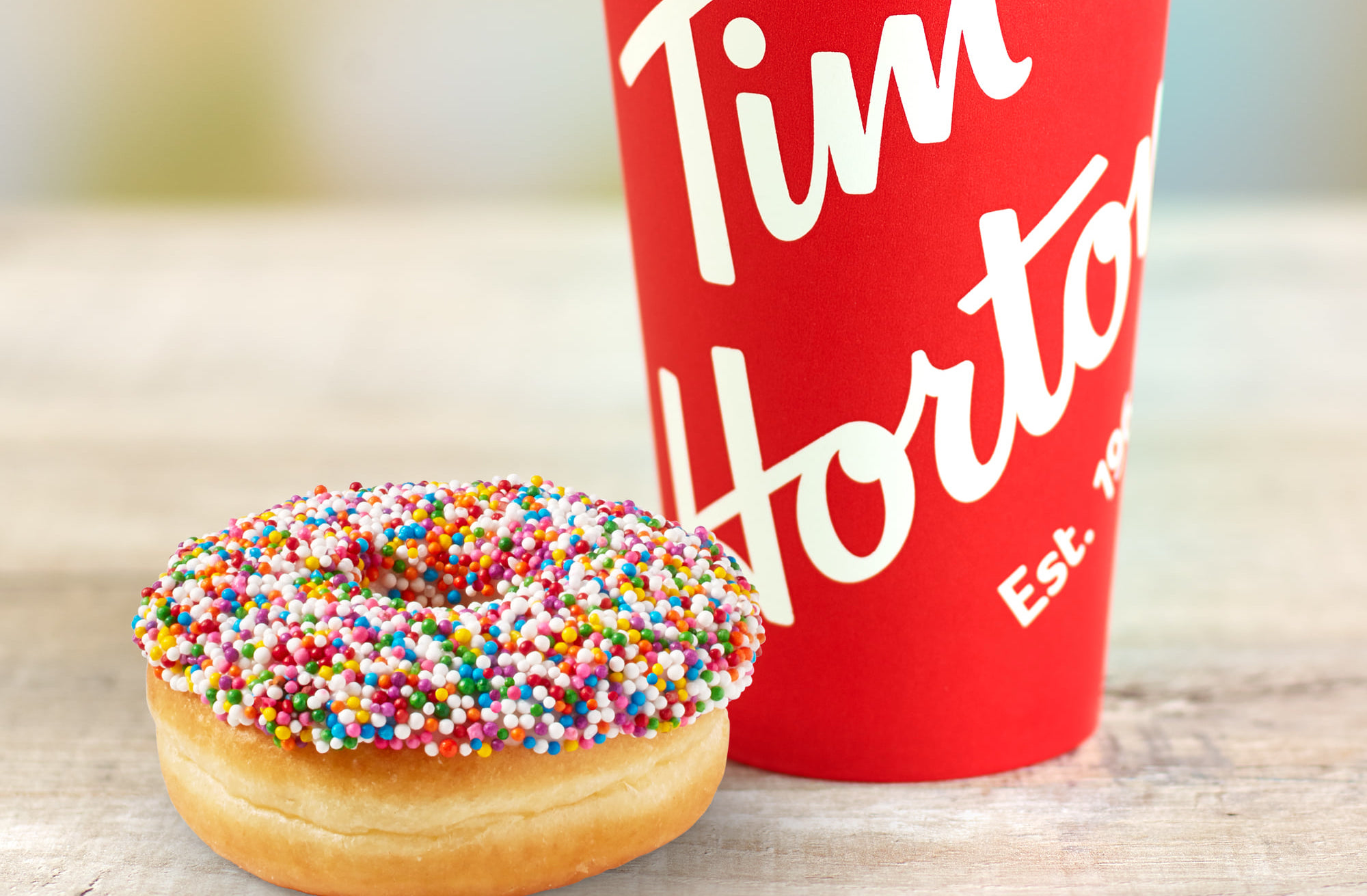 A Tim Hortons coffee and doughnut, the coffee in a red cup and the doughnut topped with sprinkles