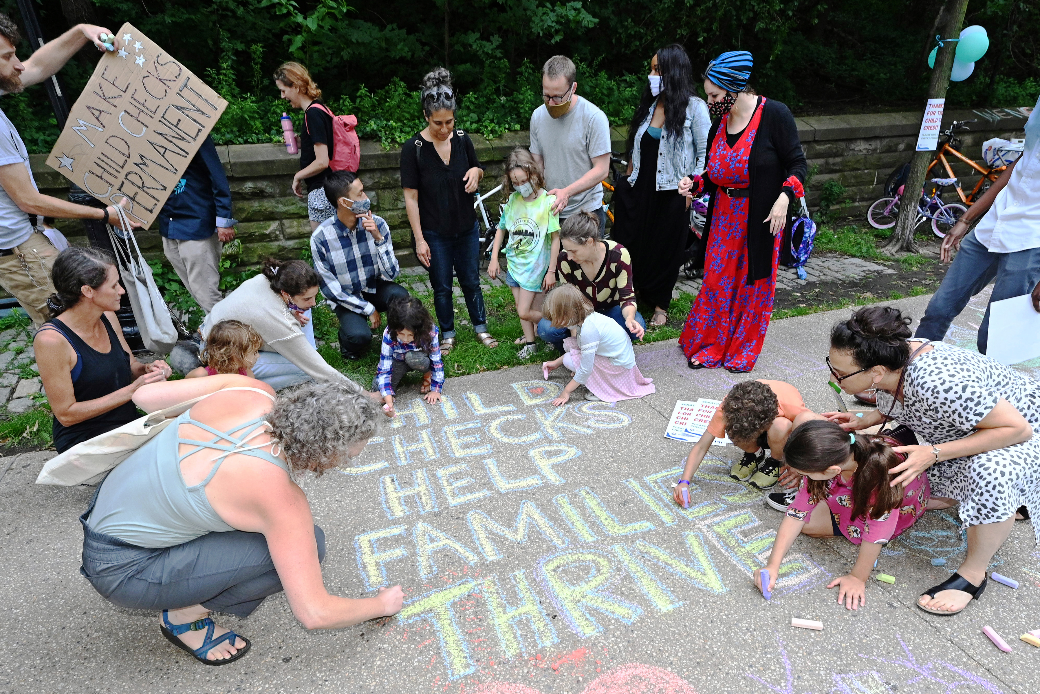 Adults and children use chalk to write “Child checks help families thrive” on the sidewalk.