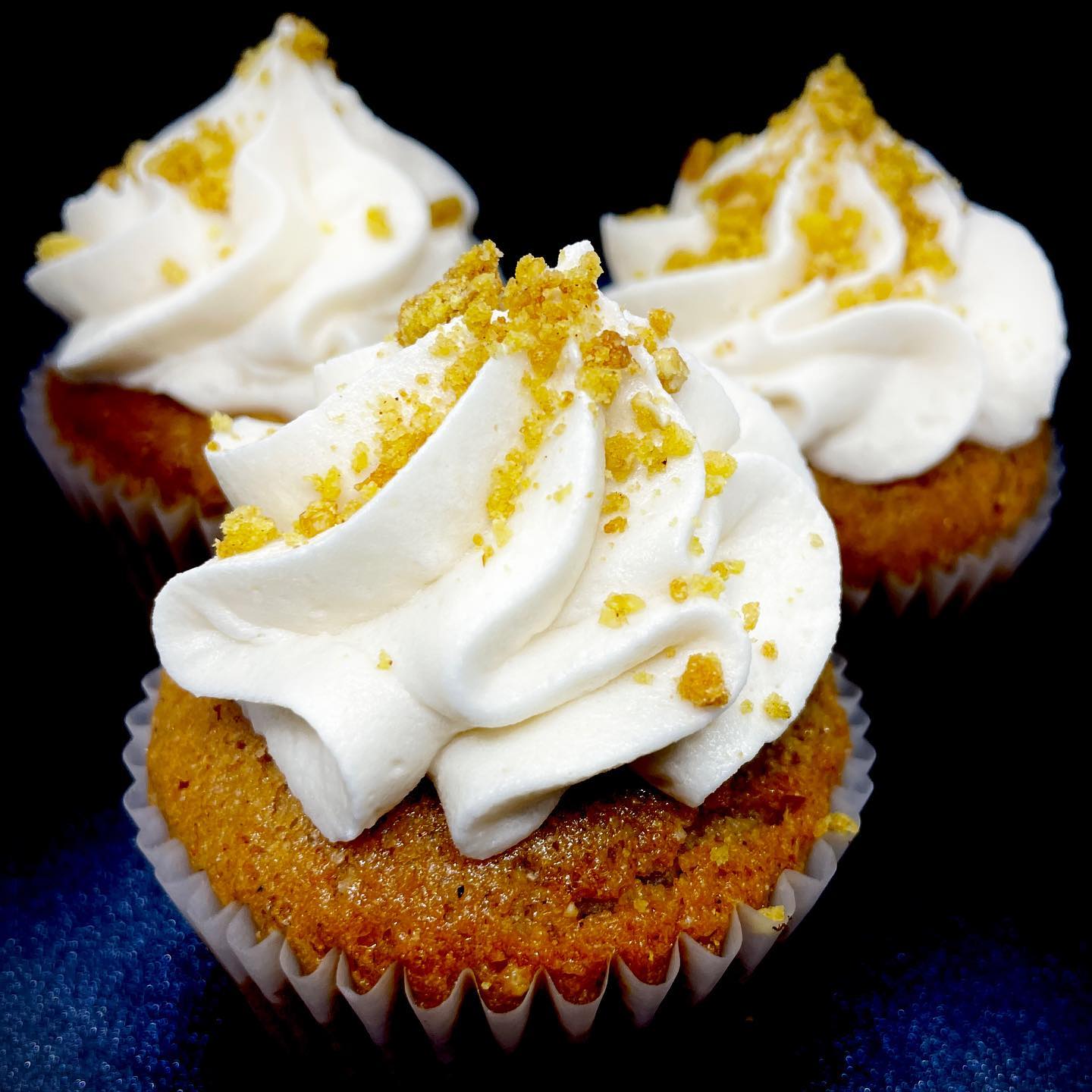 Three brown cupcakes with white frosting and yellow crumbles.