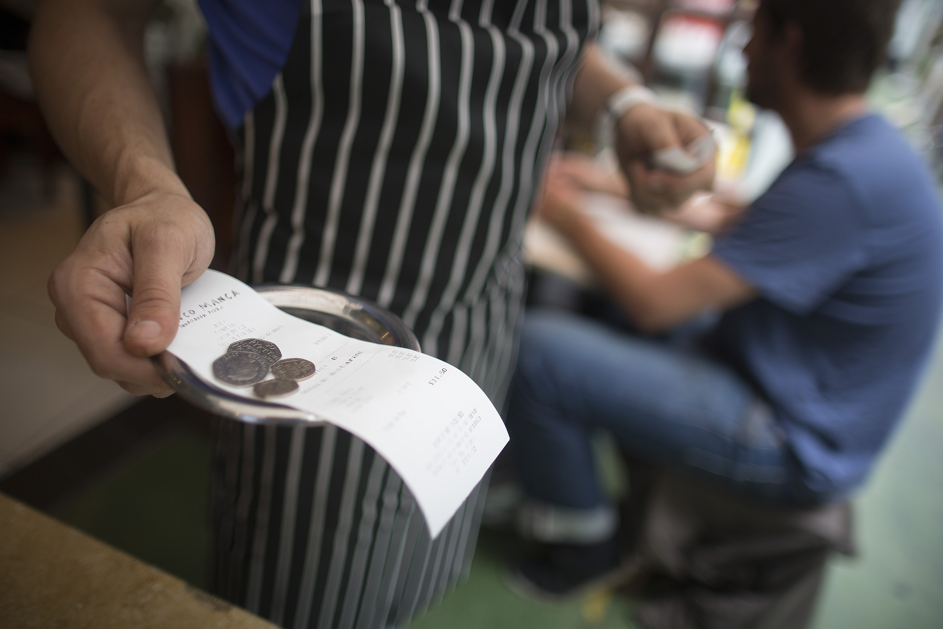 A receipt with a tip, in the form of coins, being carried away from a table by a waiter