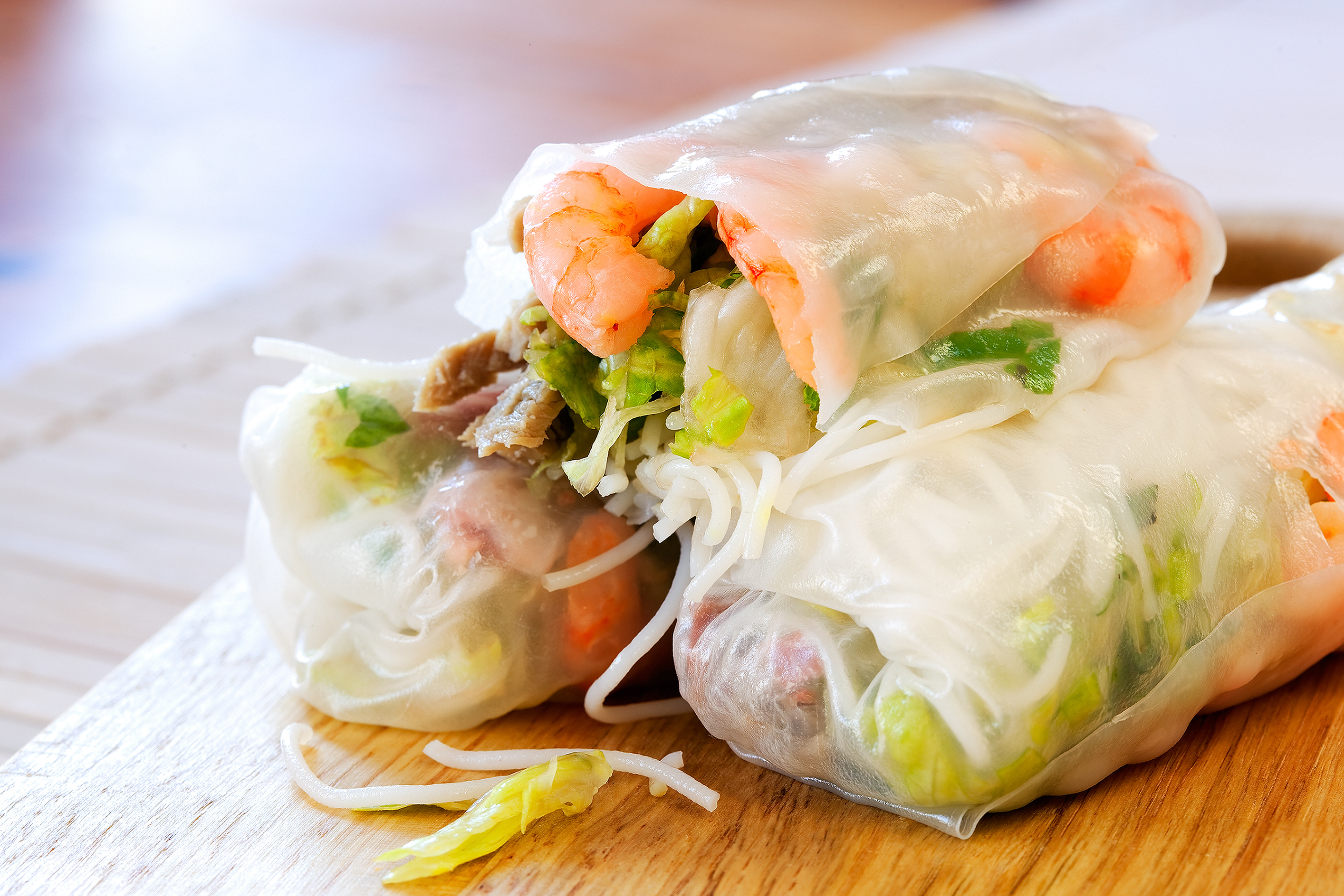 Three Vietnamese spring rolls on a board containing shrimp, vermicelli noodles, lettuce, and herbs.