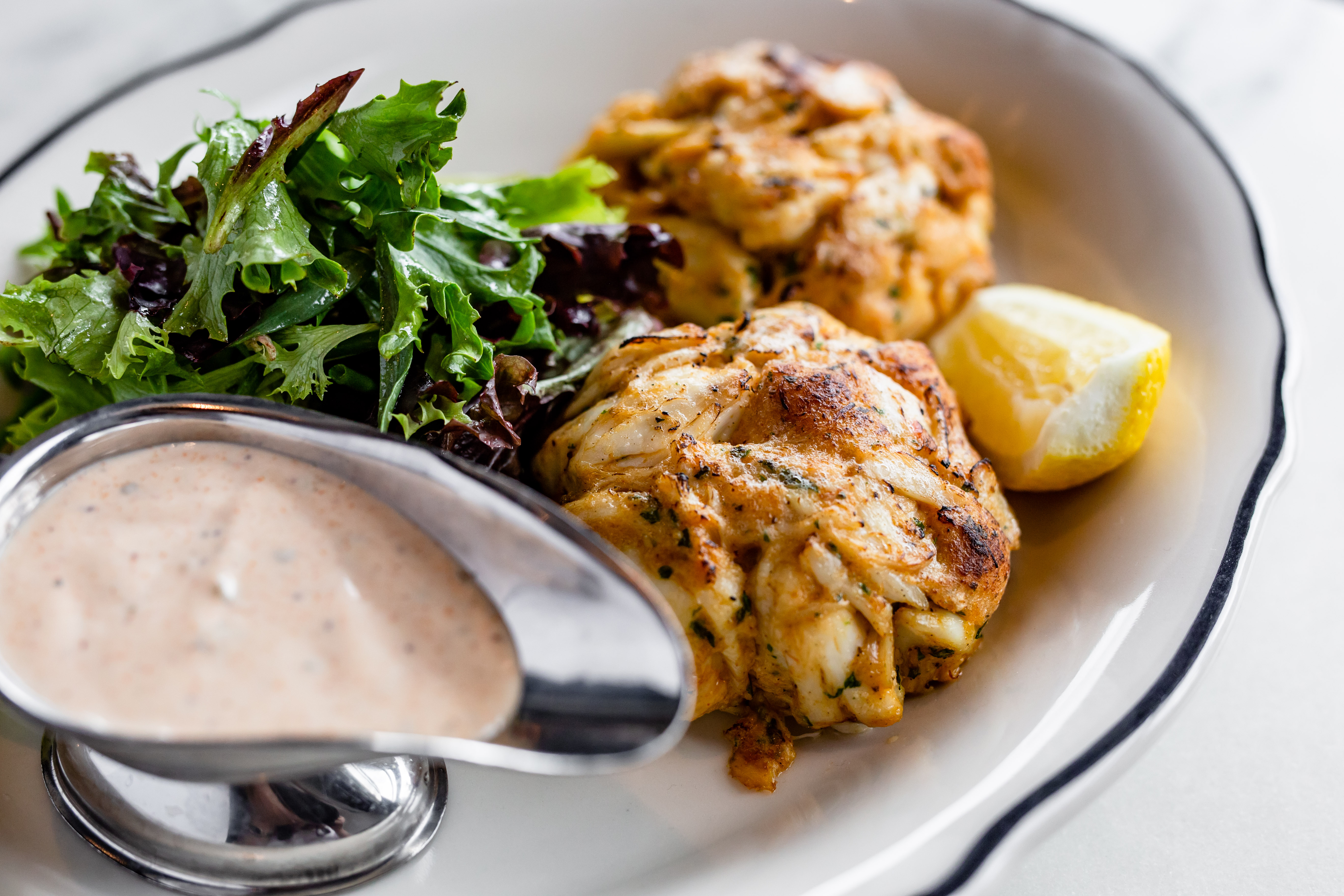 A plate of two crab cakes with a lemon and remoulade sauce.
