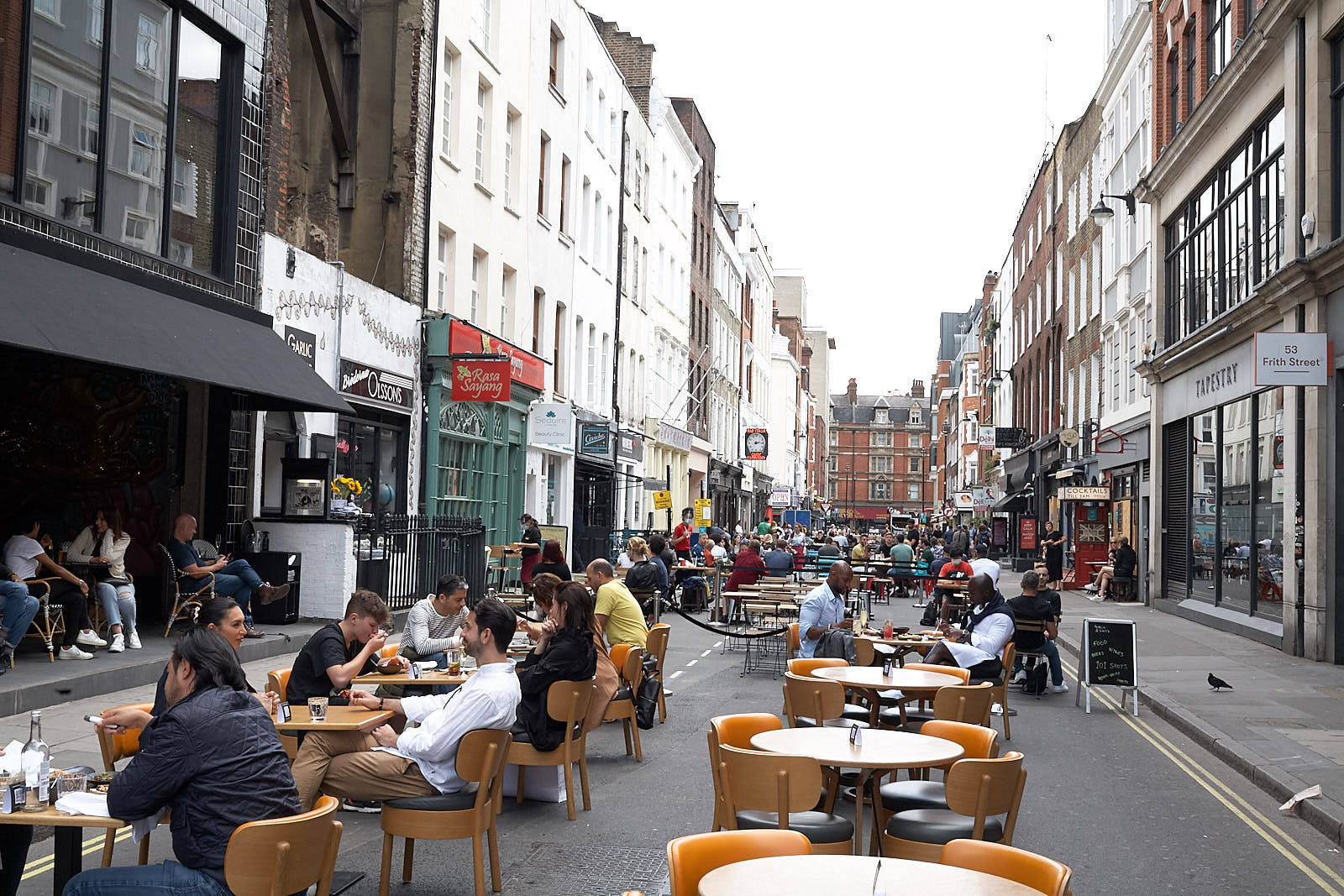 Diners sit at tables on a closed Soho street in summer 2020