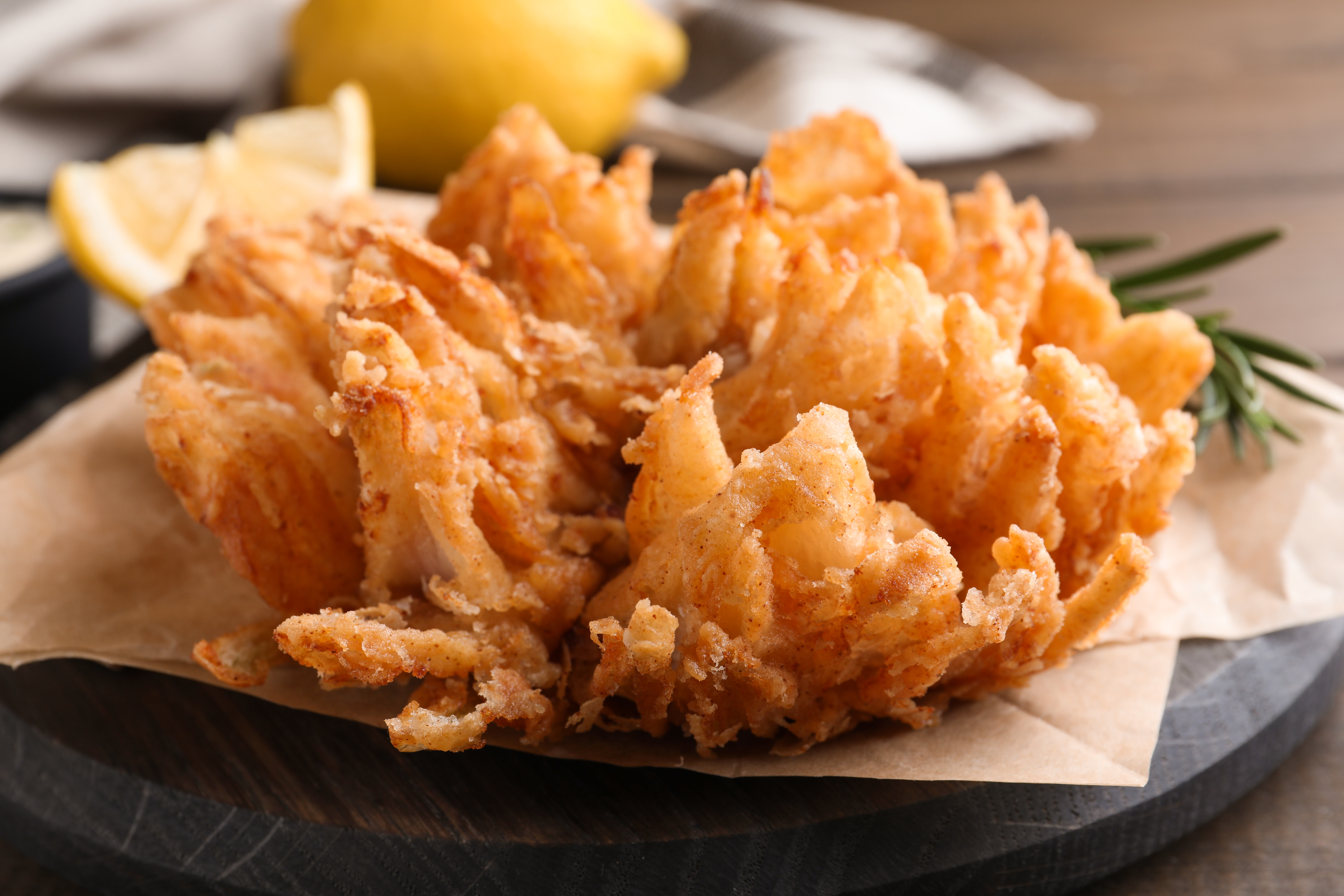 Fried onion blossom rests on paper on a slate.