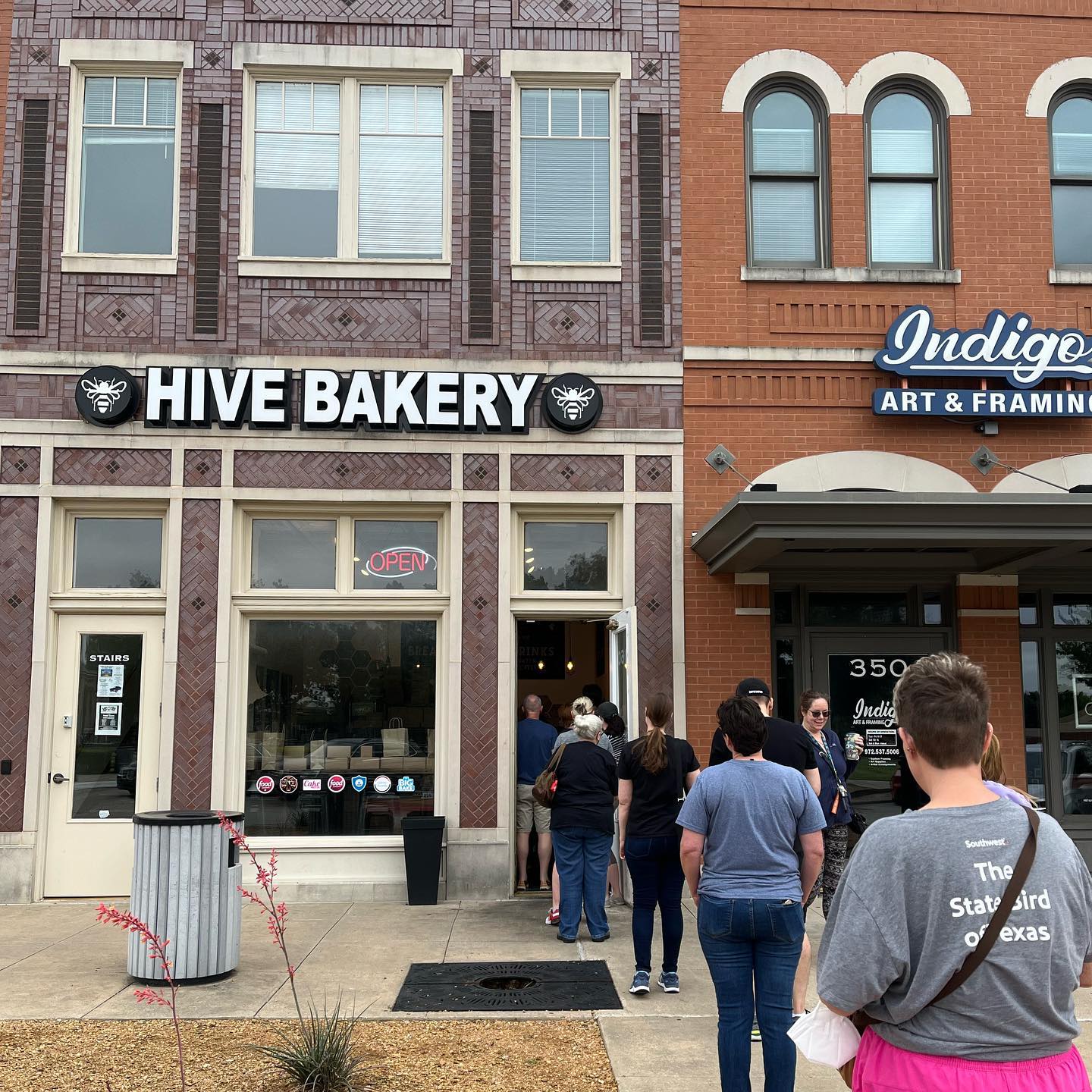 The exterior of Hive Bakery, a brick building, in Flower Mound, with a line of people waiting to make purchases.