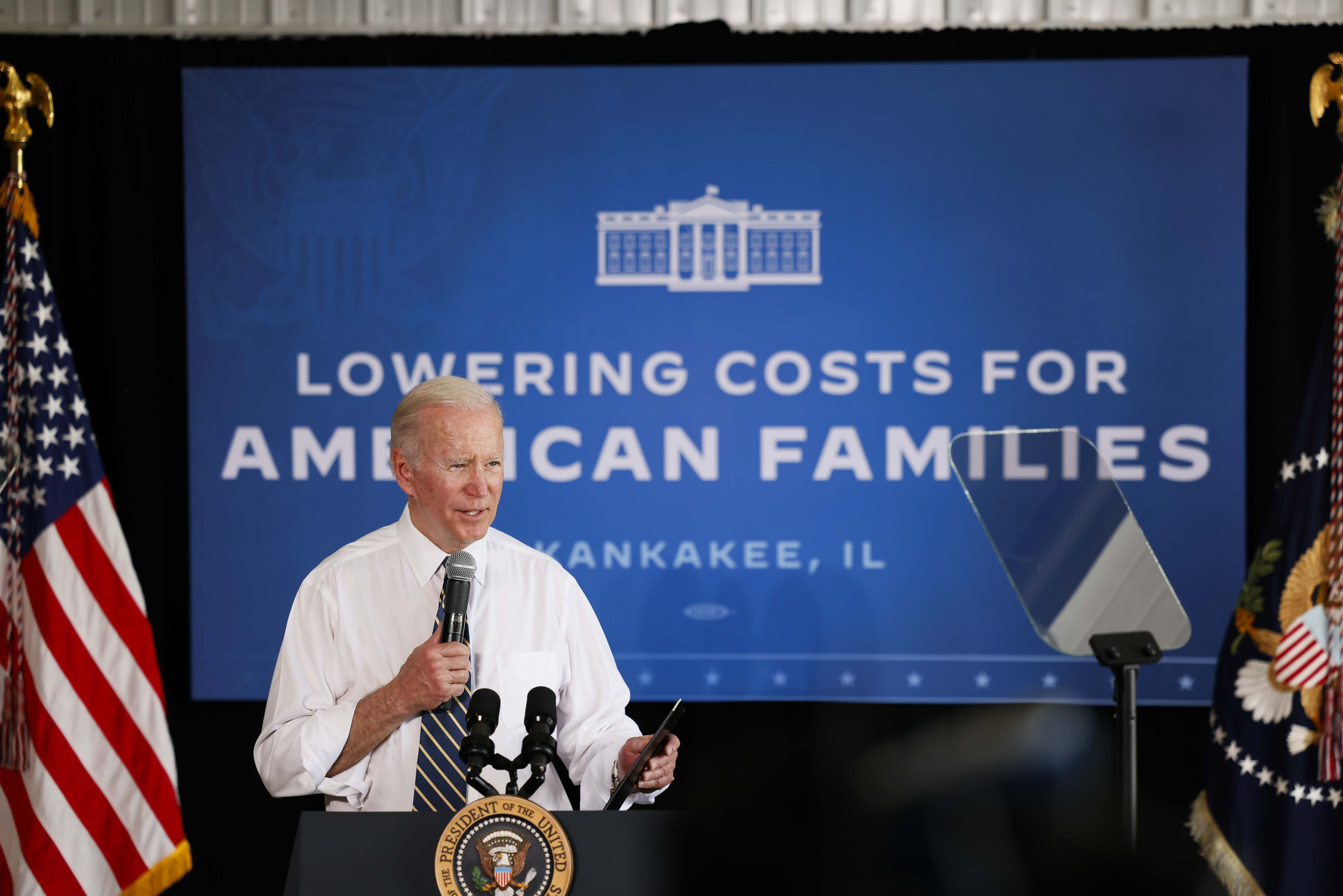 President Biden speaking into a microphone from in front of a backdrop that reads “Lowering costs for American families.”