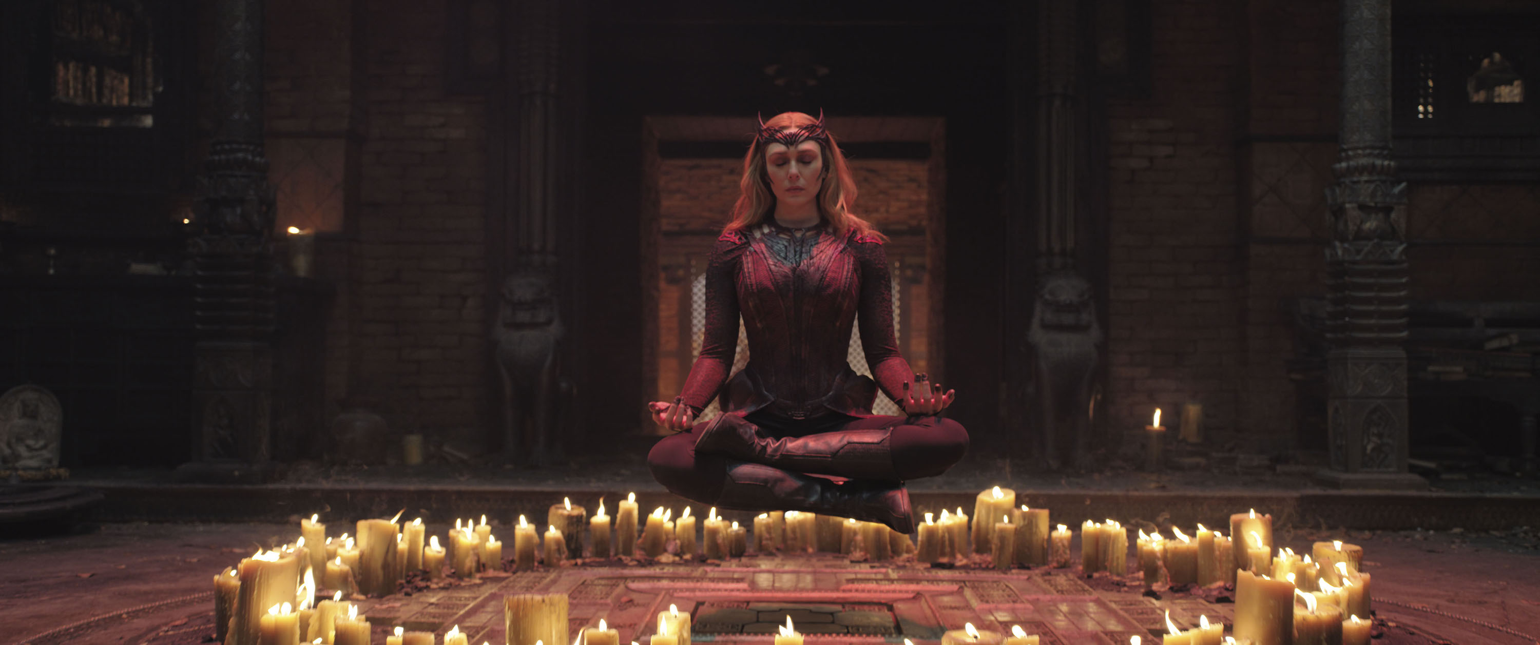 Elizabeth Olsen as Wanda Maximoff floats in the air in lotus position, eyes closed, above a circle of candles in Doctor Strange in the Multiverse of Madness.