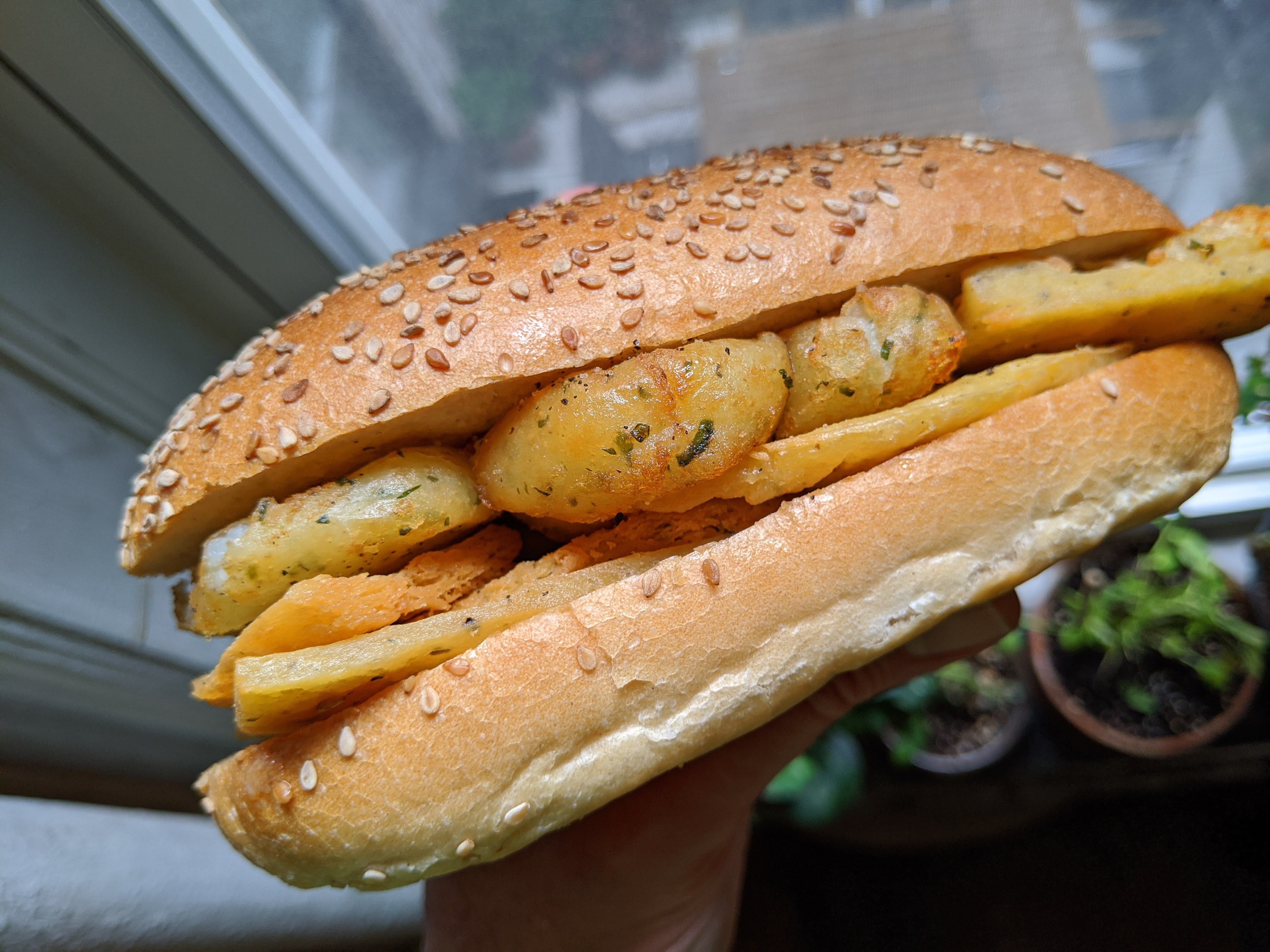 An oblong sandwich with flat browned fritters and round small potatoes.