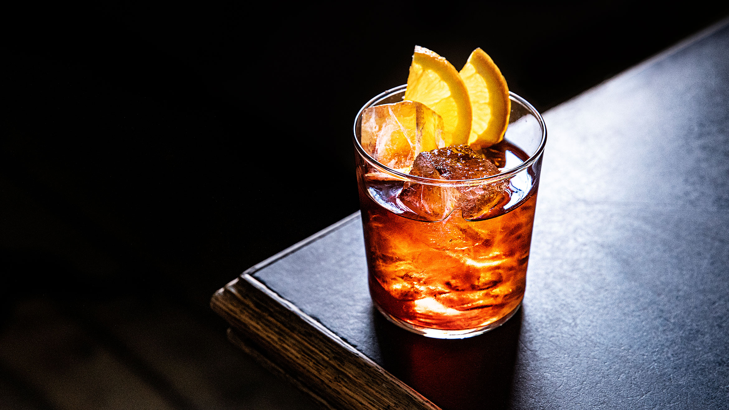 Negroni cocktail with citrus garnish on a dark-wood table.