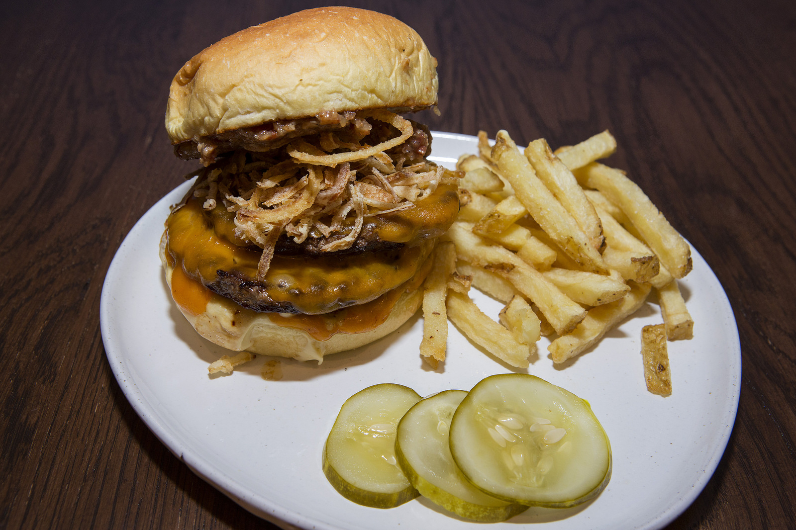 A very stuffed burger on a plate with fries and pickle slices.