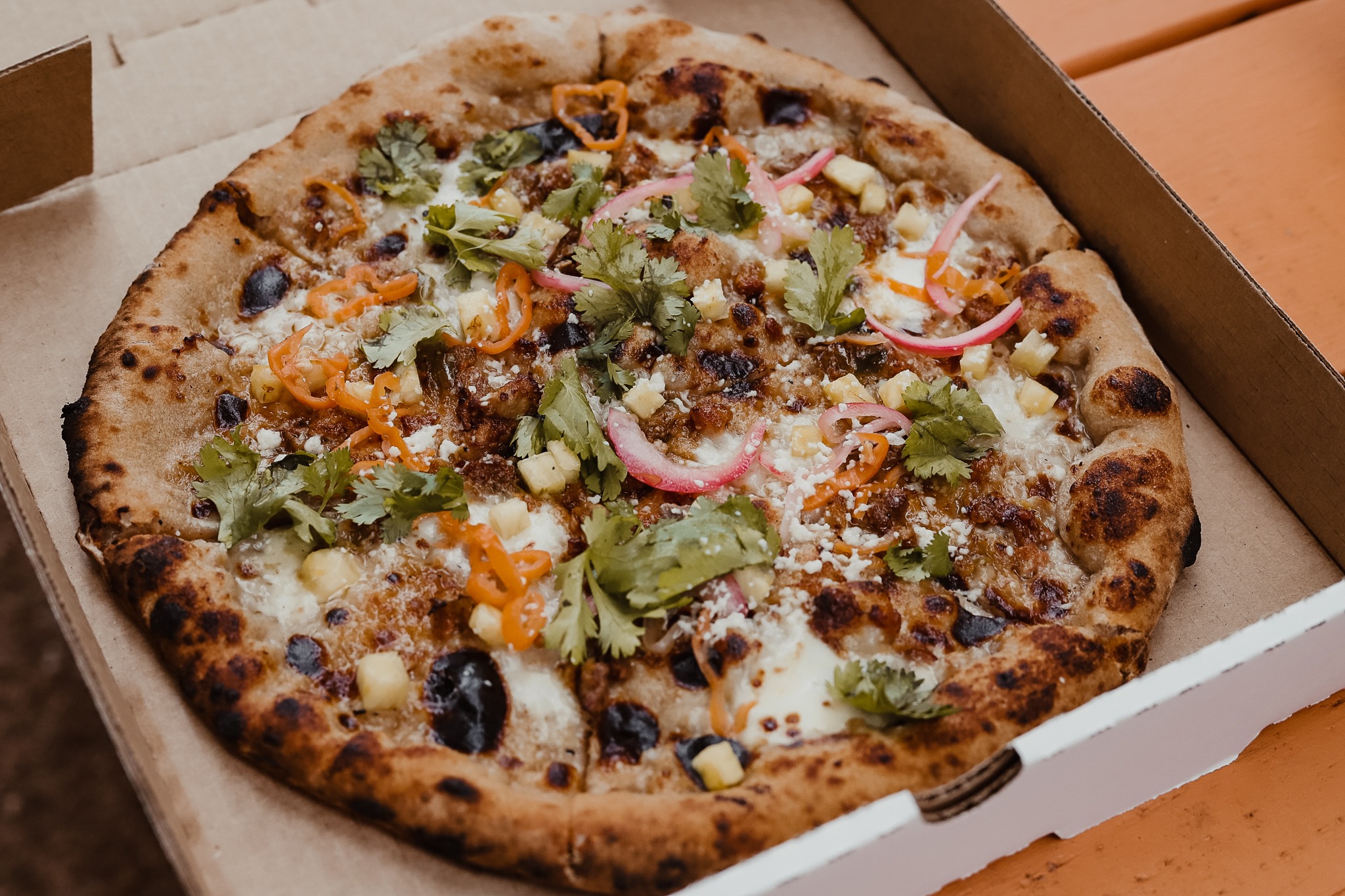 A pizza in a box with a bubbling crust and vegetable toppings from Dough Boys.