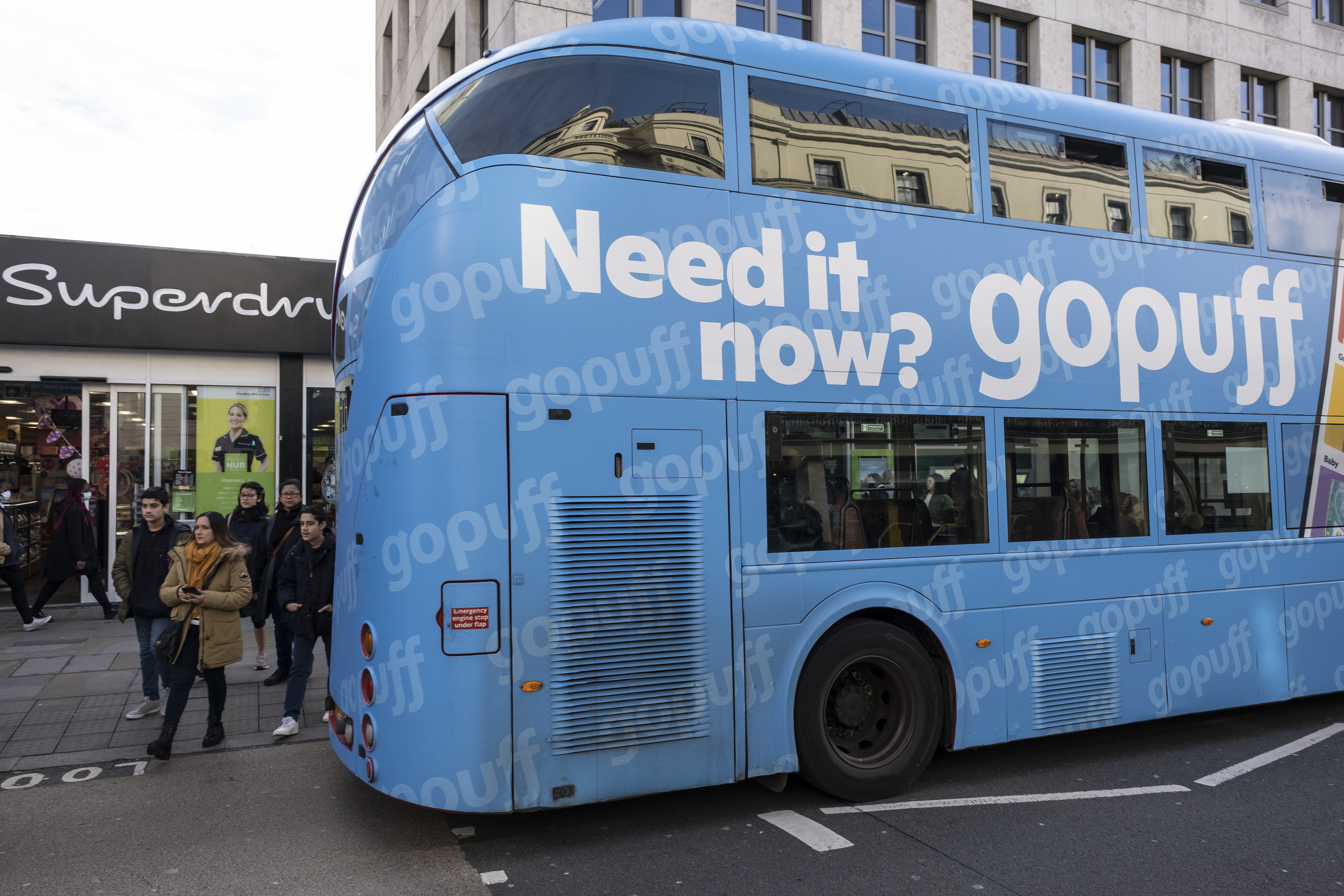 A parked double-decker bus covered by a Gopuff ad that reads, “Need it now?”