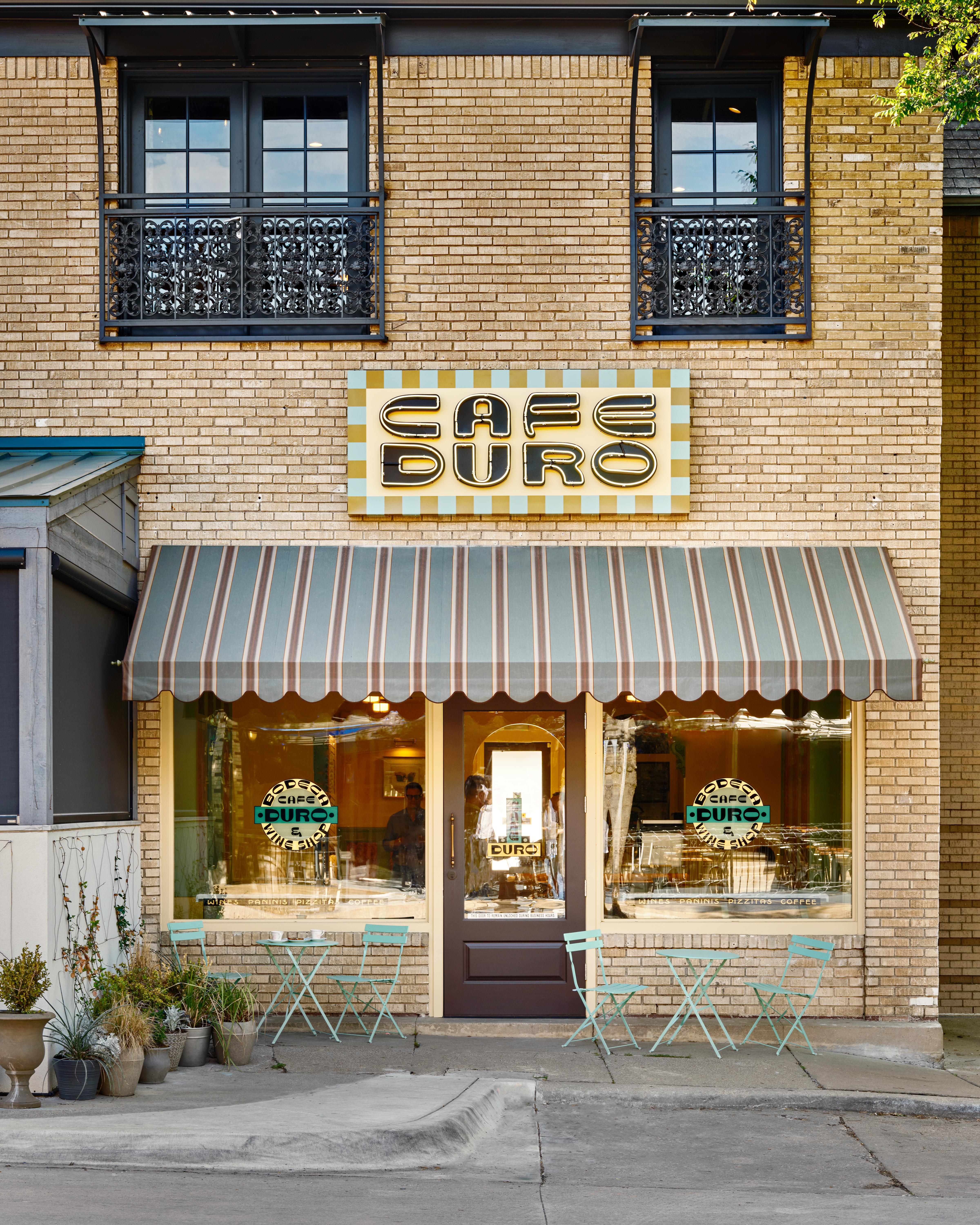 The exterior of Cafe Duro on Dallas’s Greenville Avenue has a light brick facade and a striped awning with Tiffany blue tables and chairs.