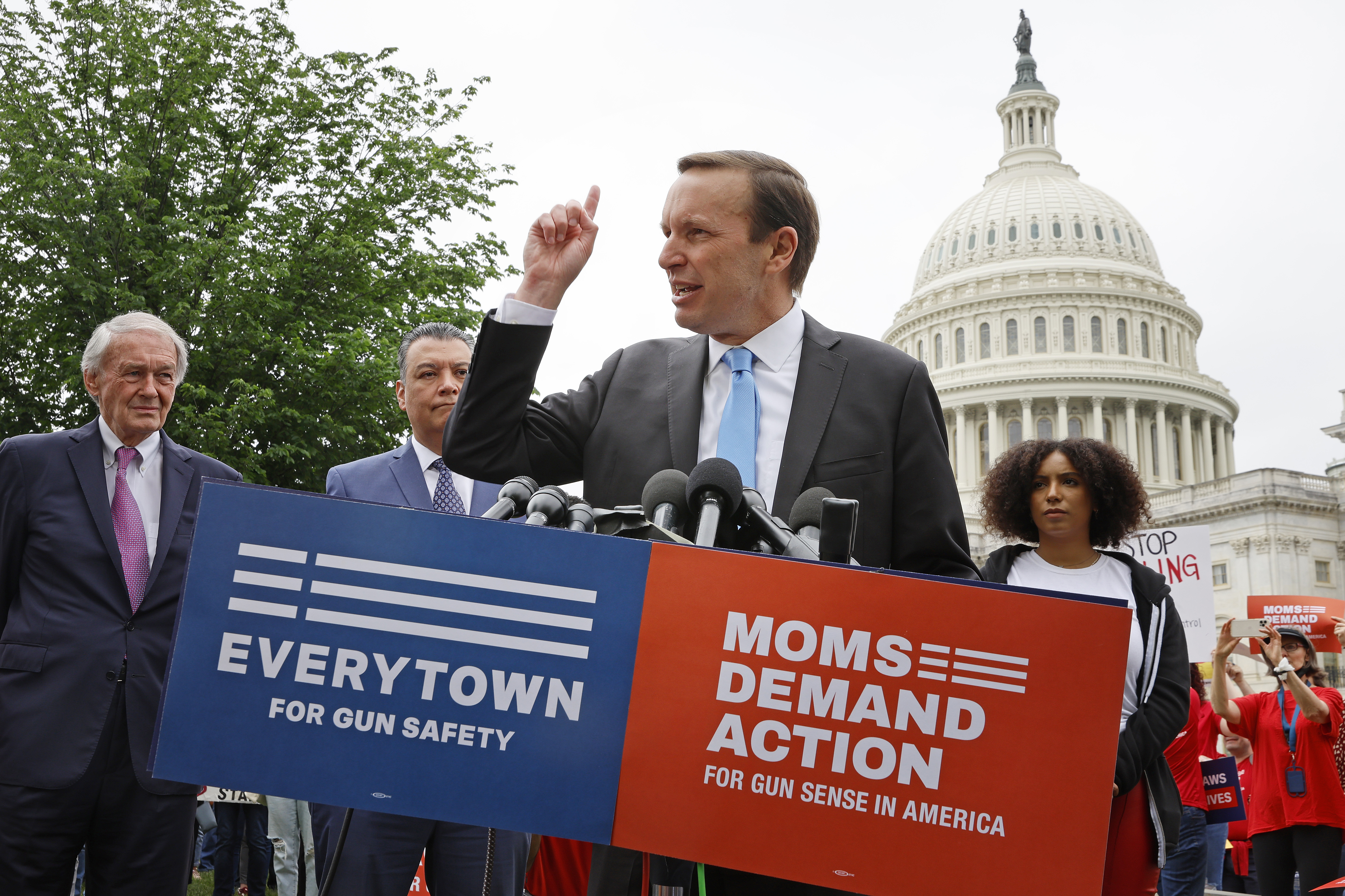 A politician gestures from behind a lectern that reads “Everytown for gun safety” and “Moms demand action for gun sense in America.” The Capitol dome is in the background.