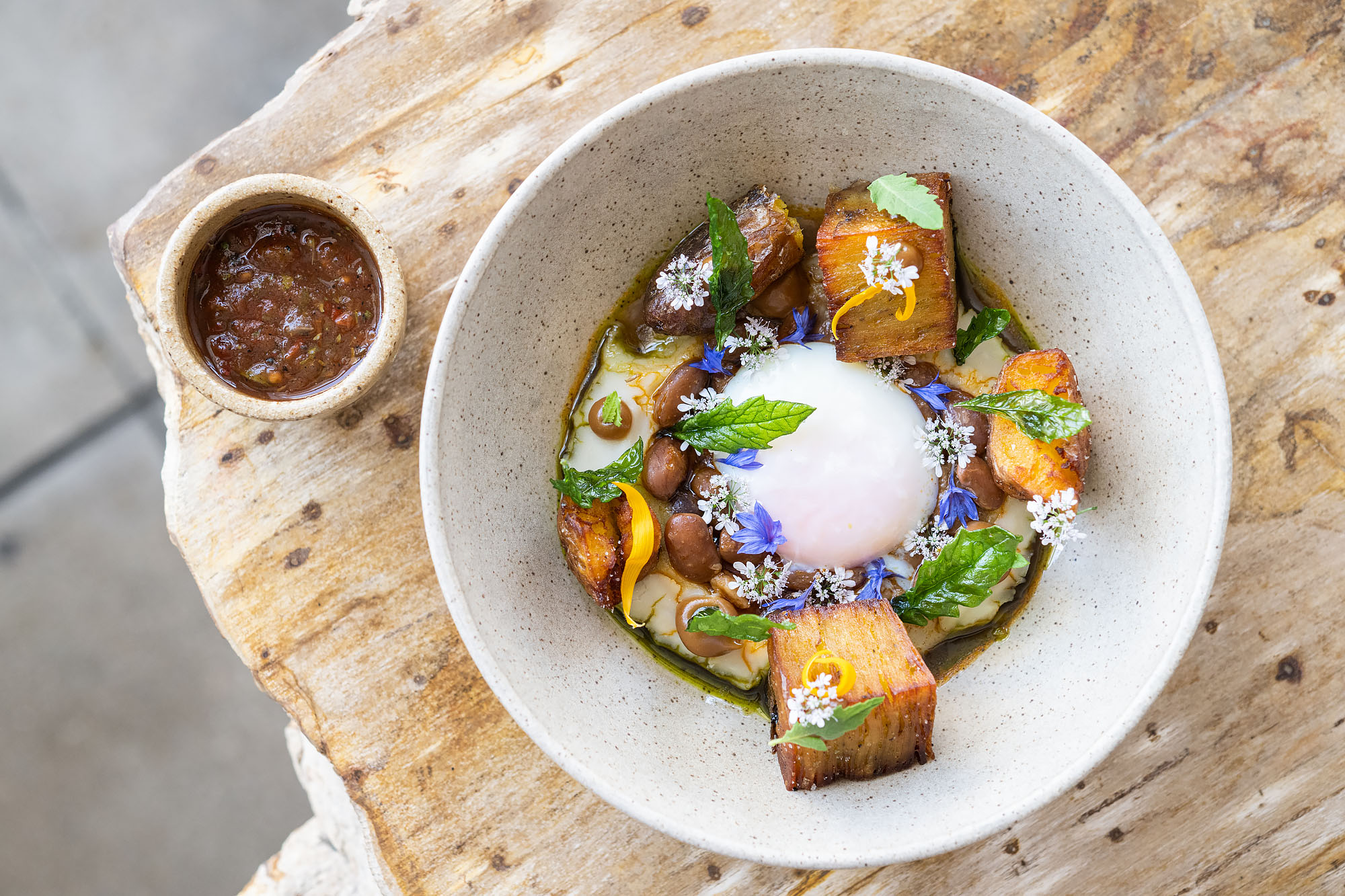 An overhead shot of a stone bowl with a poached egg and lots of herbs and cubes.