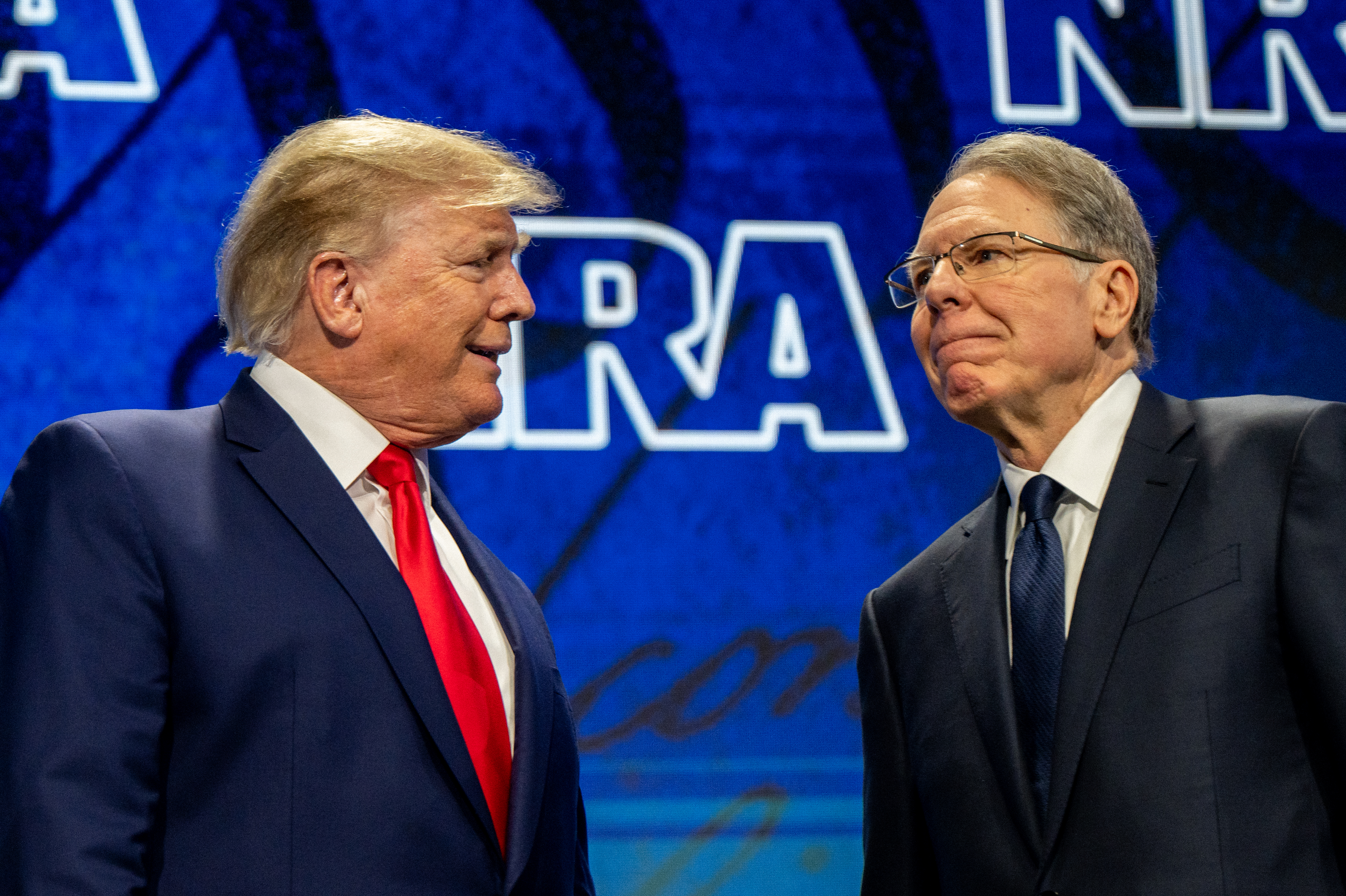 Donald Trump and NRA CEO Wayne LaPierre in front of a blue NRA backdrop on a stage.
