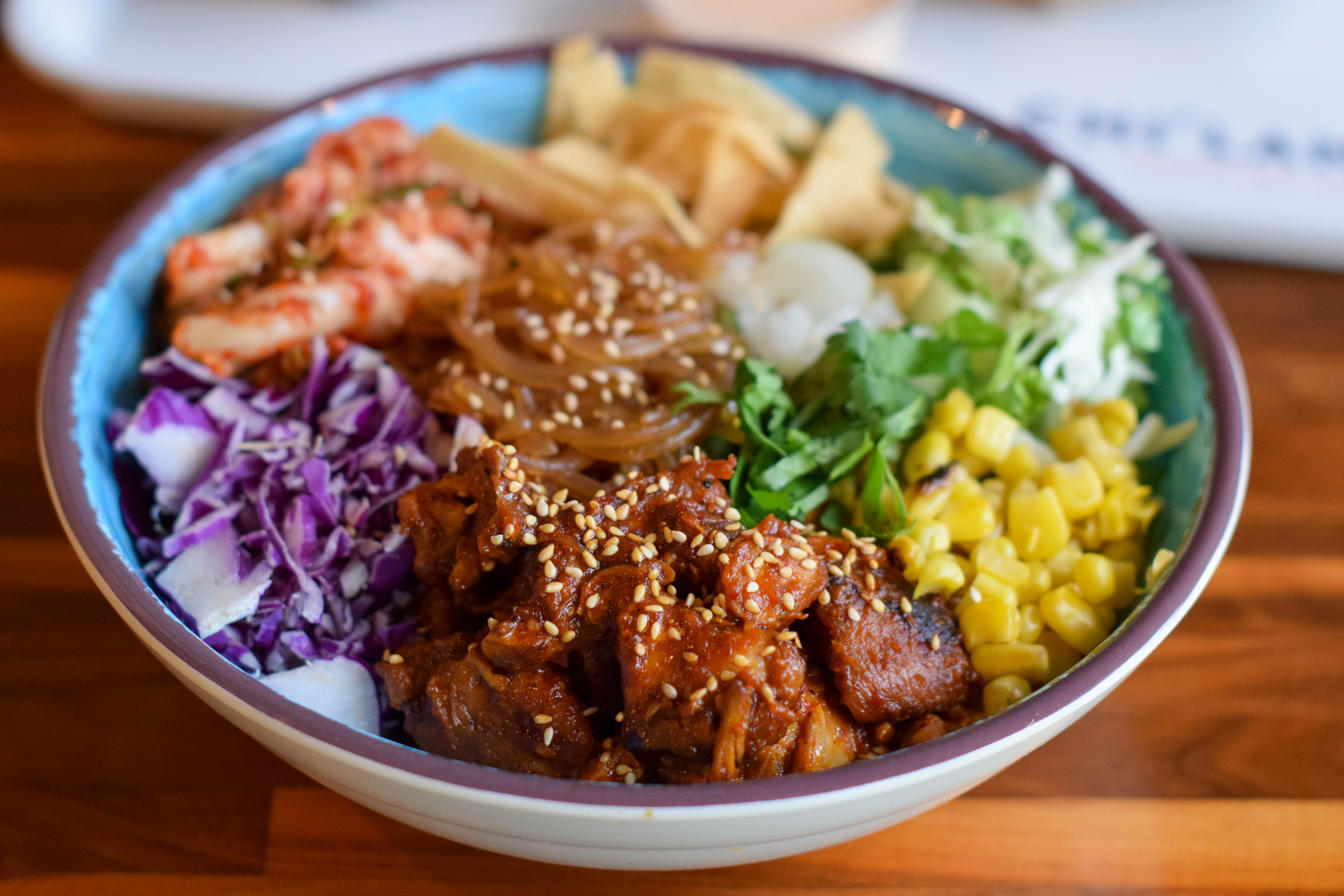 A blue bowl with meat, corn onions, cabbage, and kimchi 