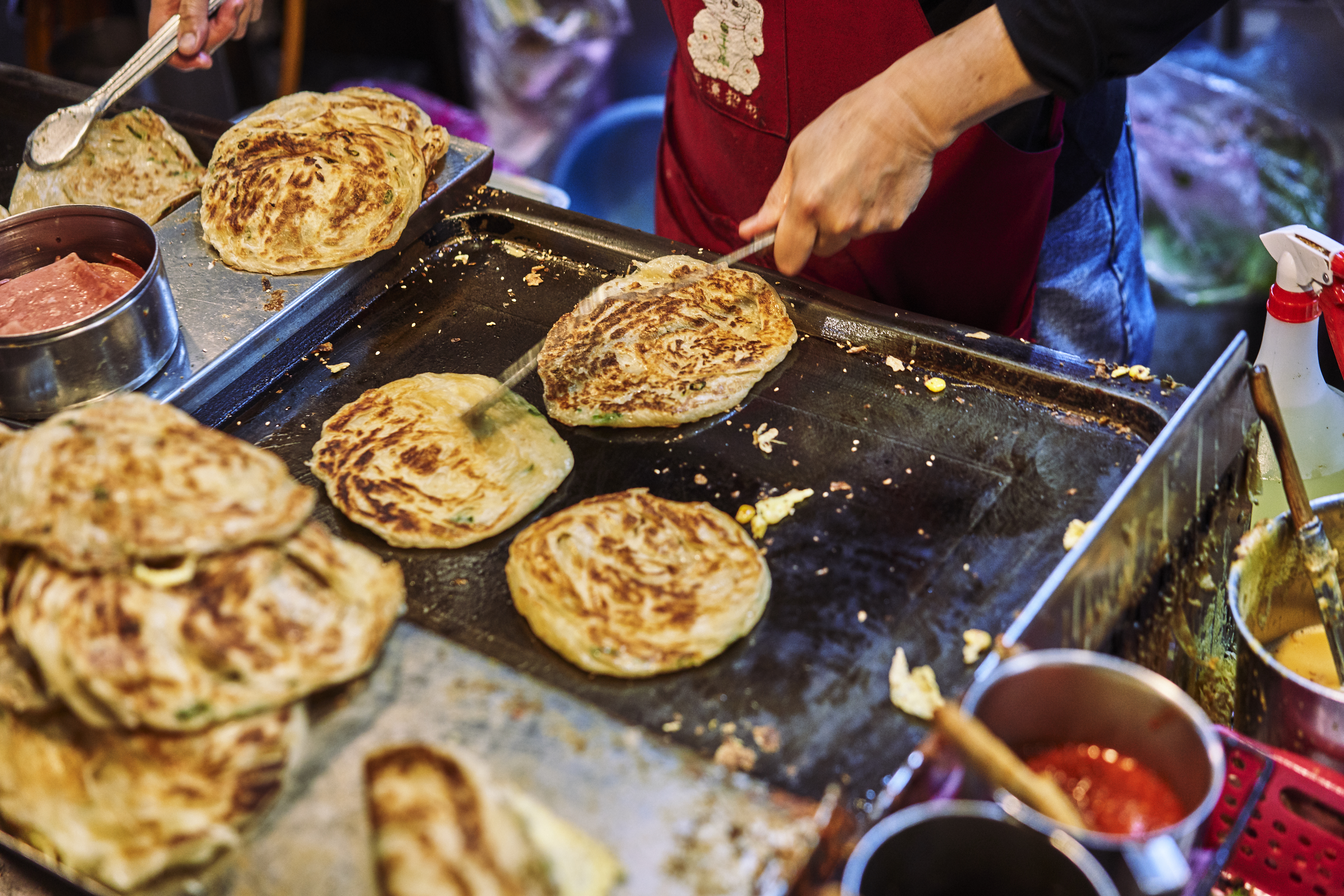 A worker flips scallion pancakes on the griddle at a street food stand.