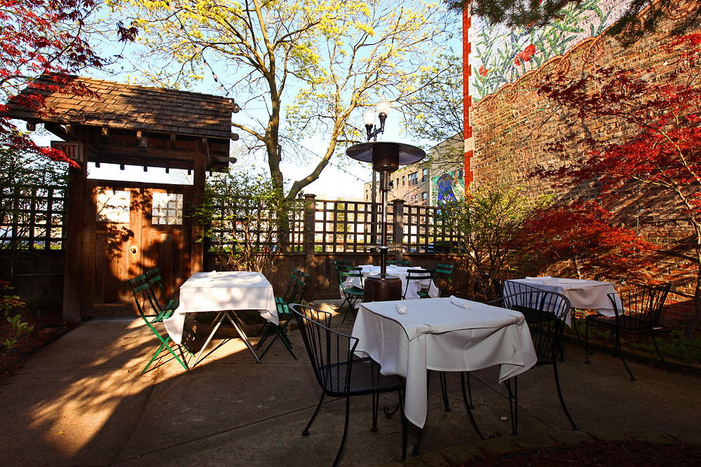 A sun-filled patio filled with tables covered in white clothes. Ivy climbs the brick wall on the right.