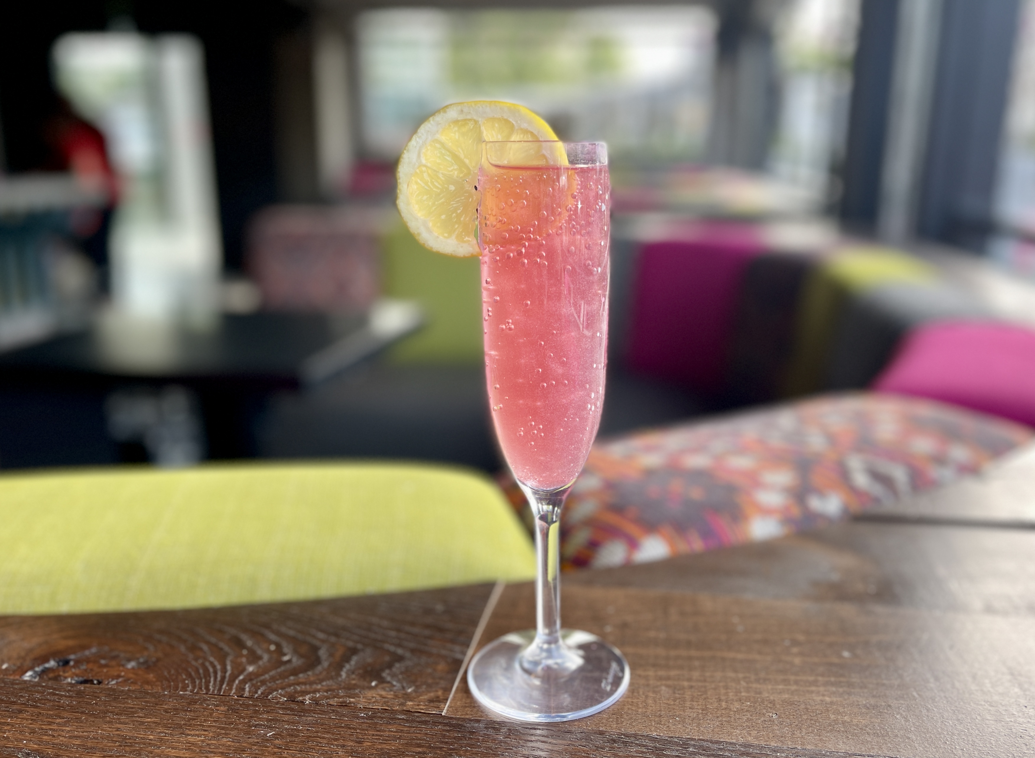 Fizzy “Pretty in Pink” cocktail in a champagne glass with lemon slice as a garnish.