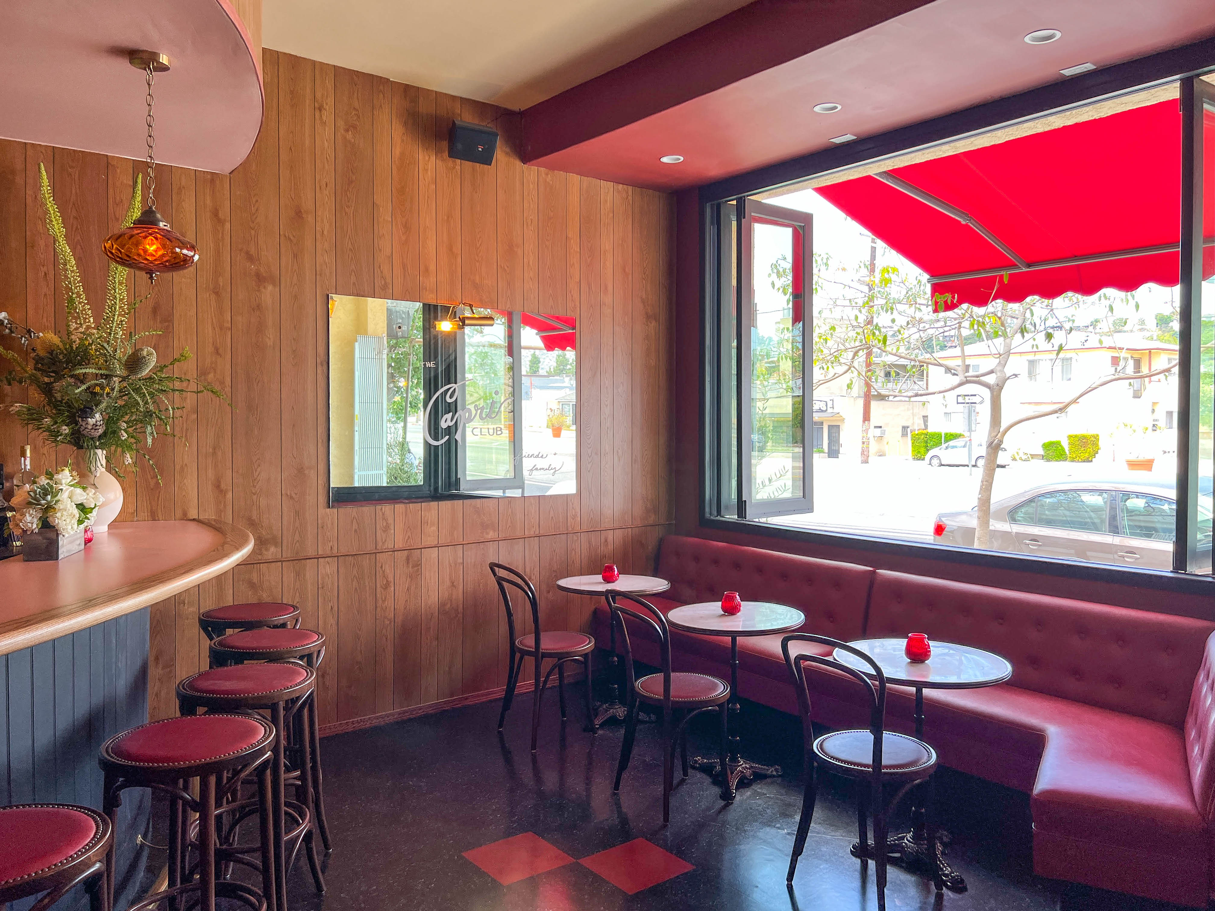 A corner look at a new bar with wood paneling and red booths, at daytime.