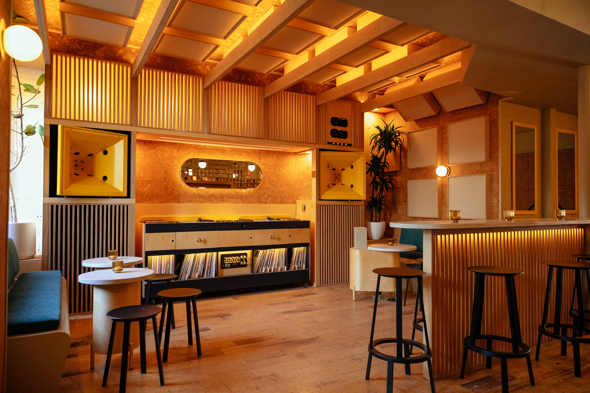 A wood paneled room is filled with records and small tables with black barstools.