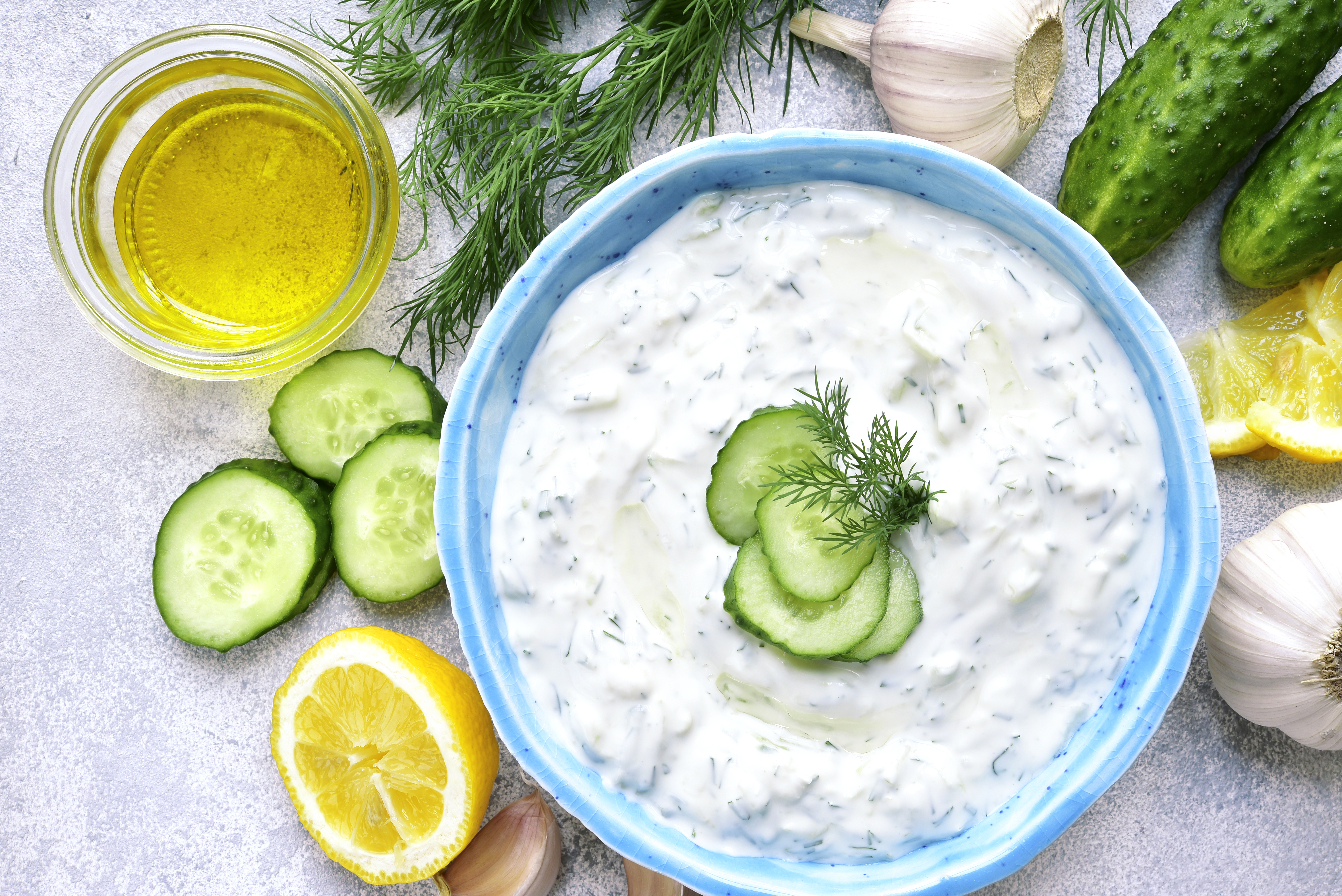 A bowl of tzatziki, surrounded by cucumbers, lemons, and garlic.
