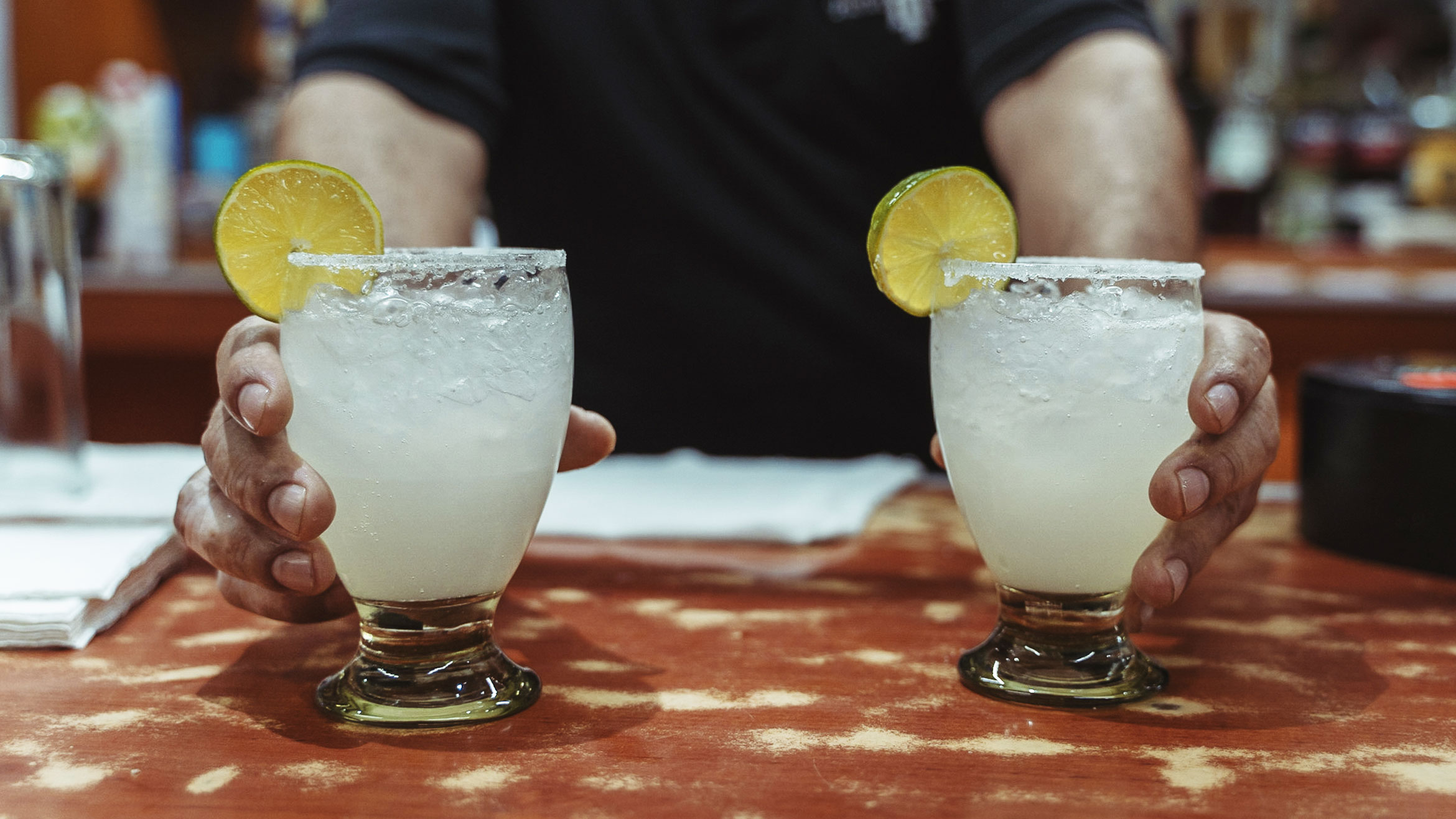 A bartender presents two margaritas