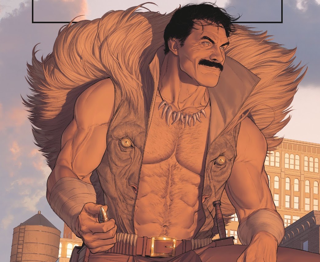 Kraven the Hunter stands on a rooftop, smiling slightly, holding a large bullet in his hand, in his open vest crowned with a lion’s mane. His muscles and chest hair are lovingly rendered, in Might Valkyries #2, Marvel Comics (2021).