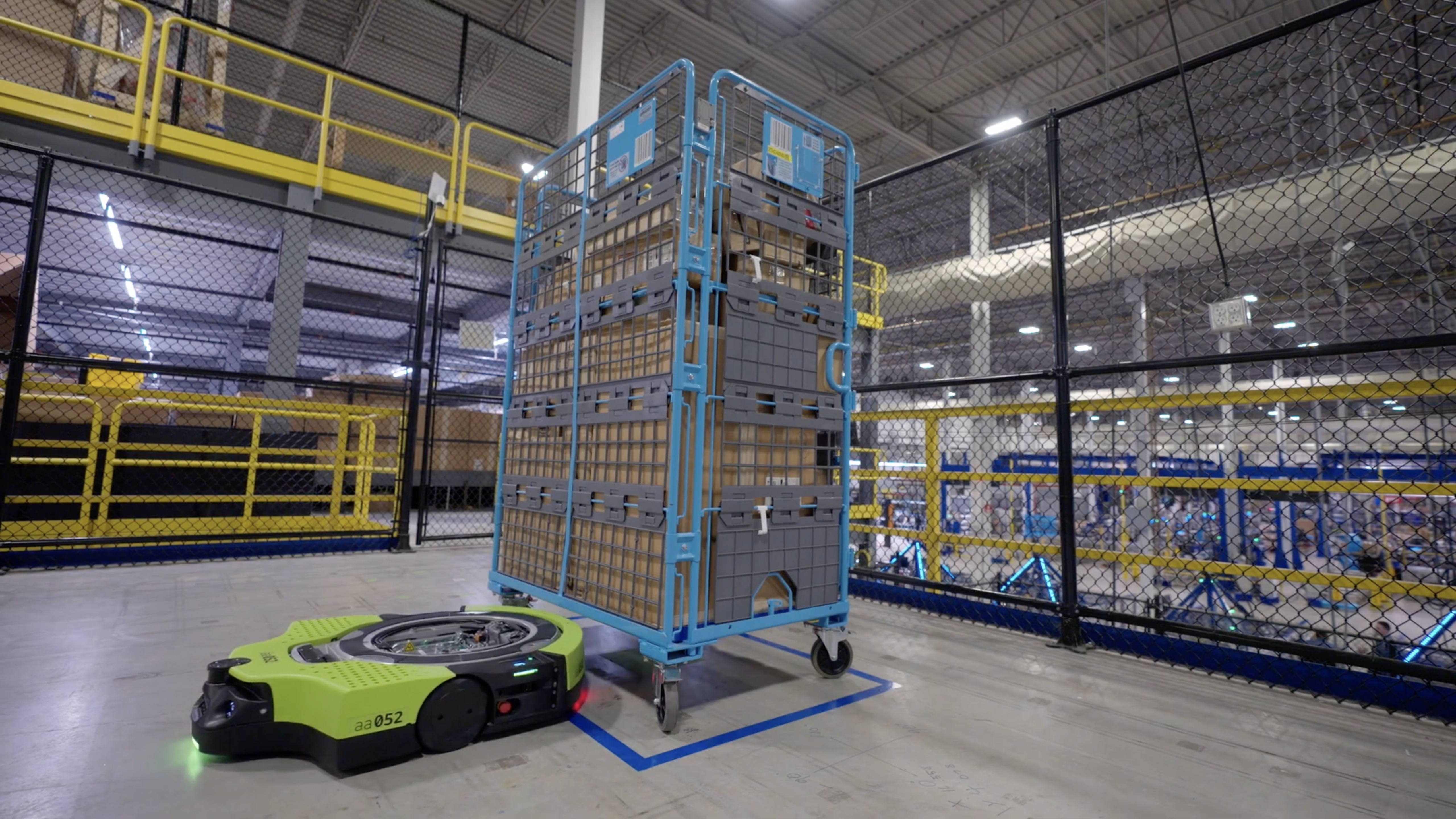 Image of a green robot sliding out from under a big metal cart filled with boxes.