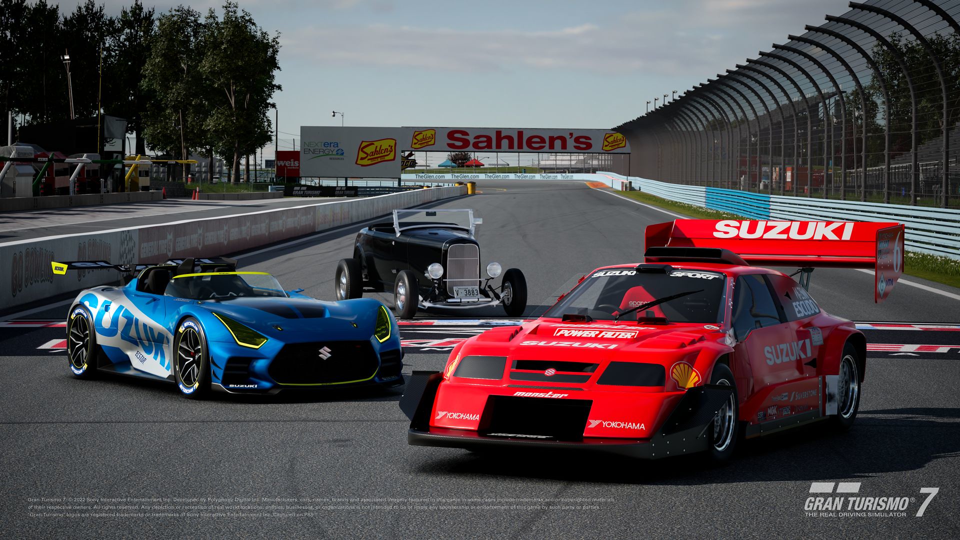 Gran Turismo 7 - three legendary cars, made up of two Suzuki race cars and the 1932 Ford Roaster, posed at a racing arena’s finish line.