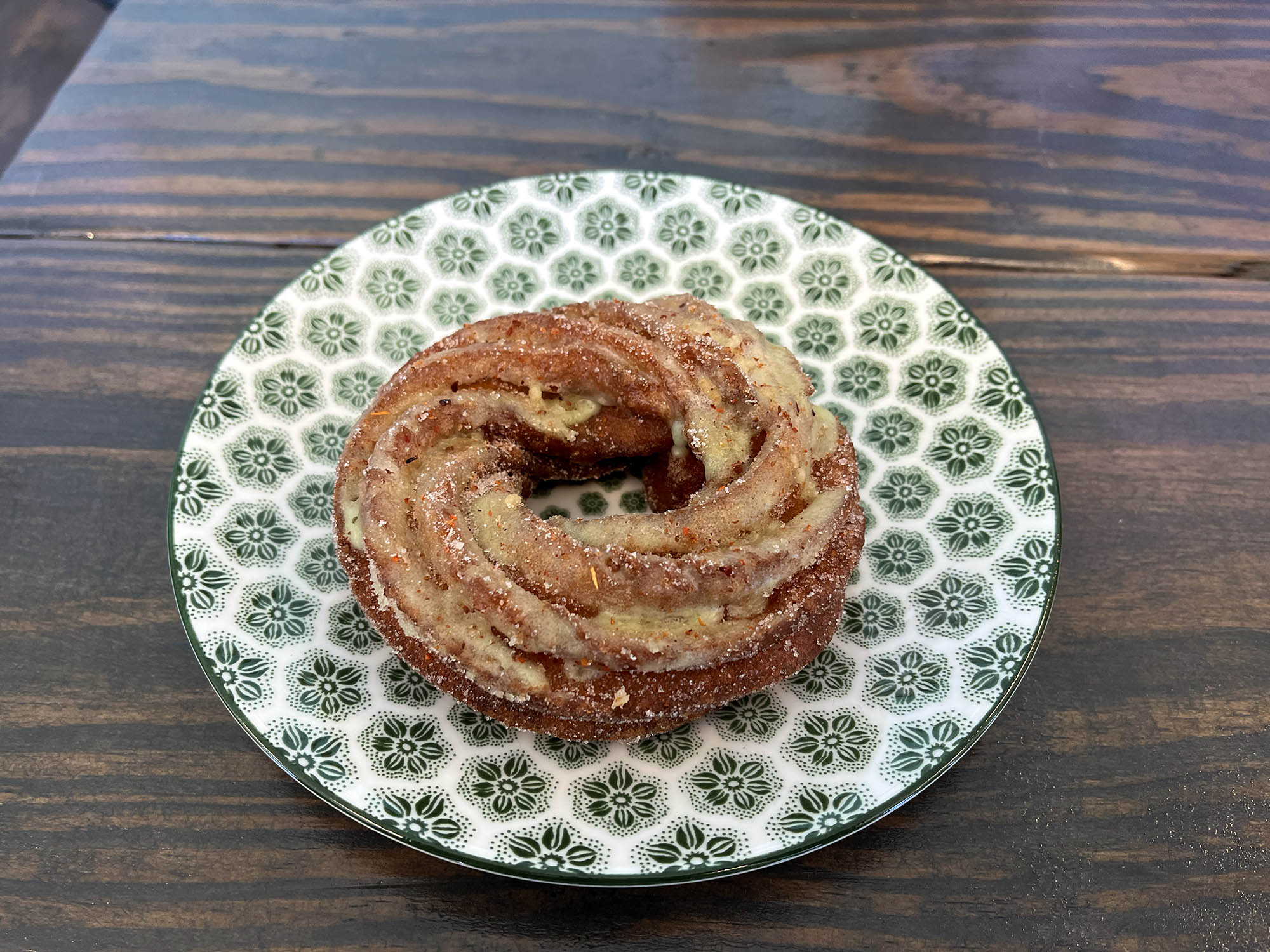 A round cruller on a green-and-white plate.