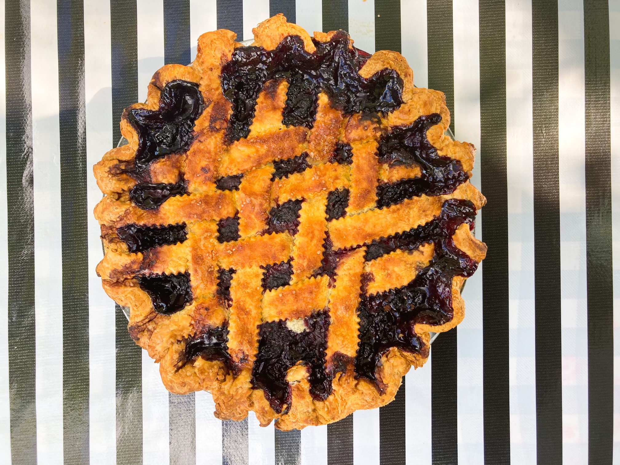 A lattice-topped marionberry pie sits on a black-and-white striped tablecloth at the outdoor tables at Lauretta Jean’s in Portland, Oregon.