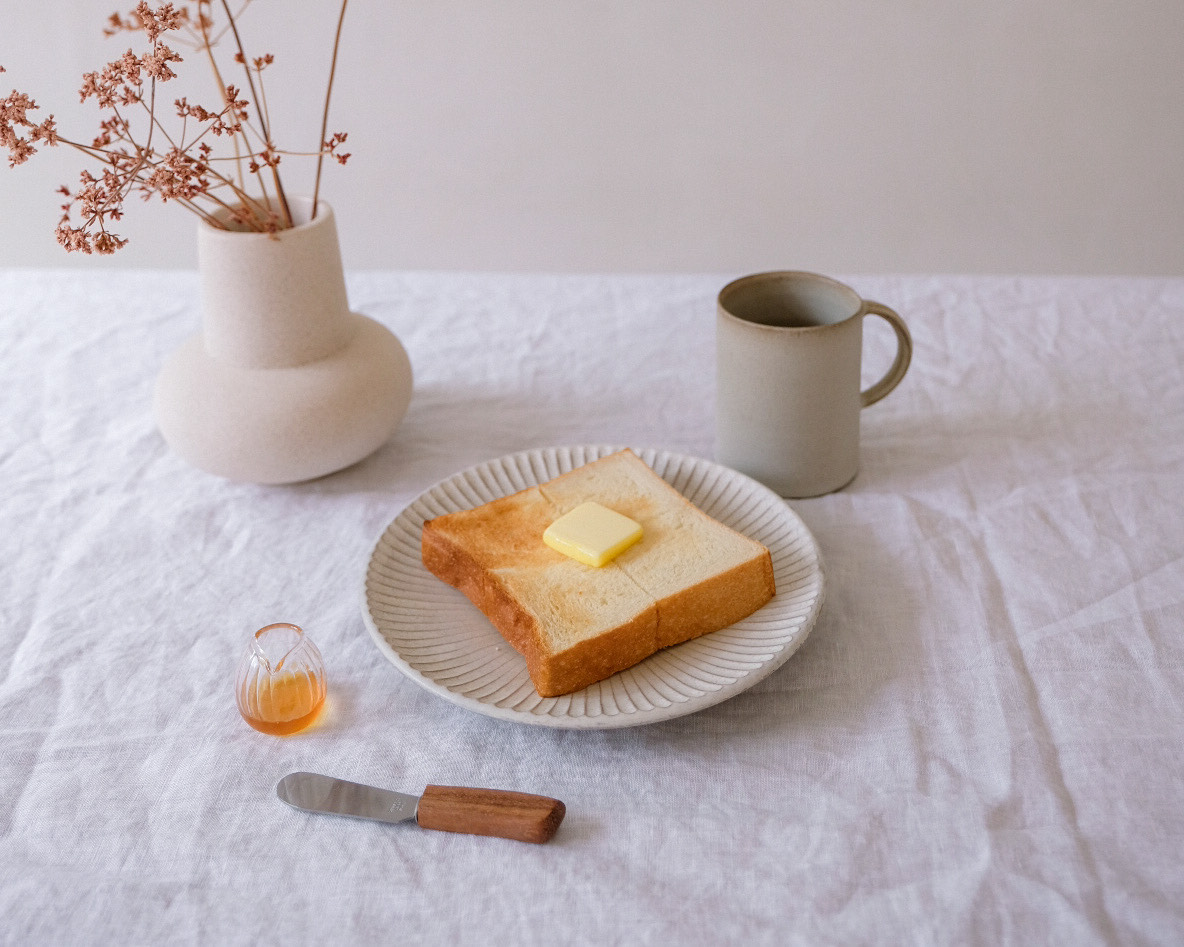 A slice of buttered bread with coffee and a flowers in a vase.