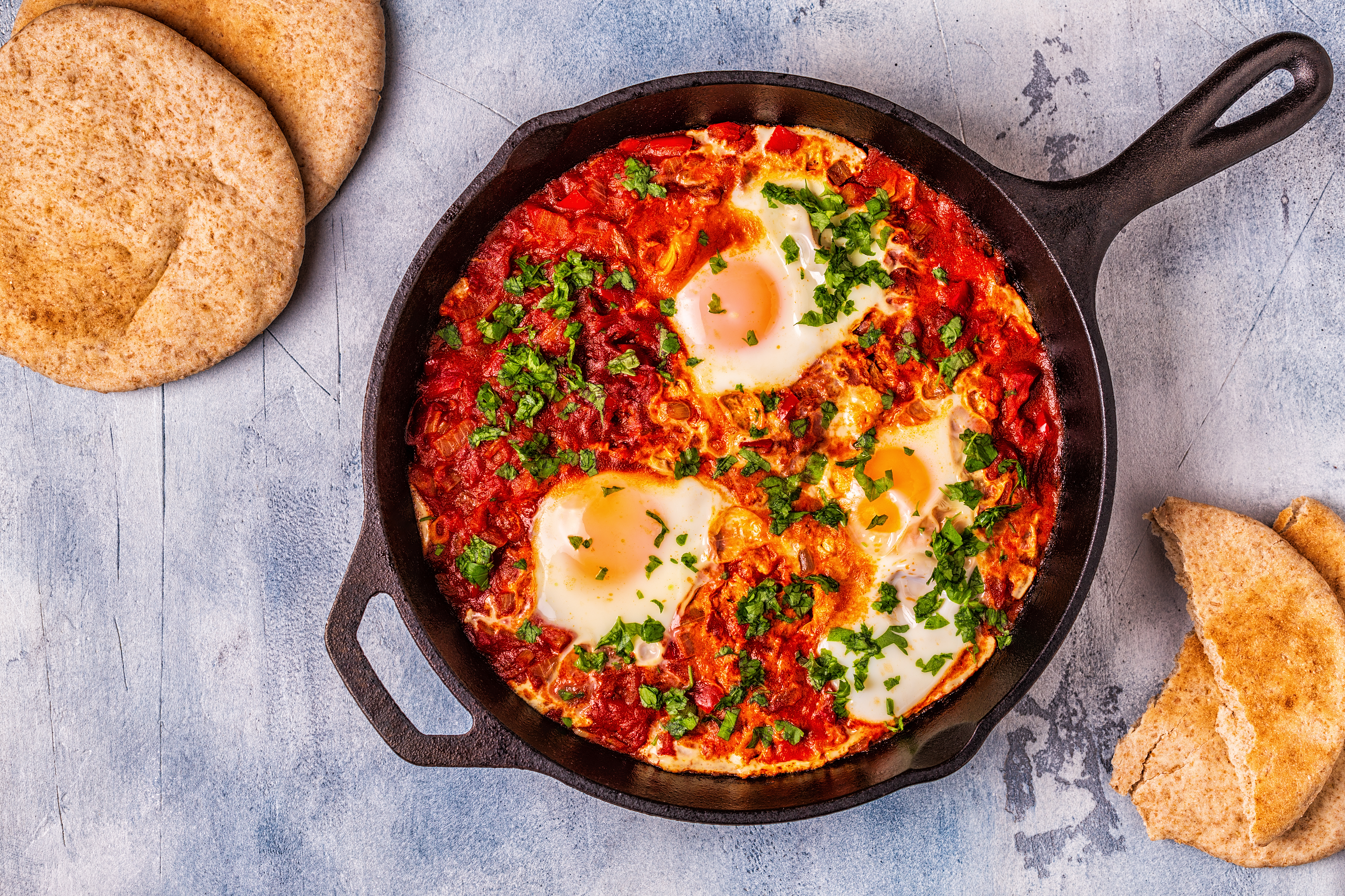 An overhead shot of a cast iron pan with shakshuka and eggs and torn pita.